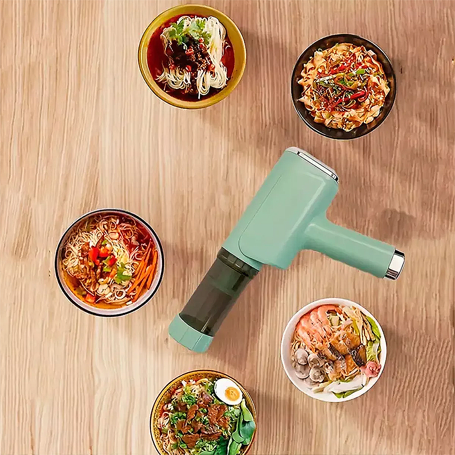 Un aspirapolvere portatile verde acqua è circondato da ciotole di noodles e ingredienti su una superficie di legno.