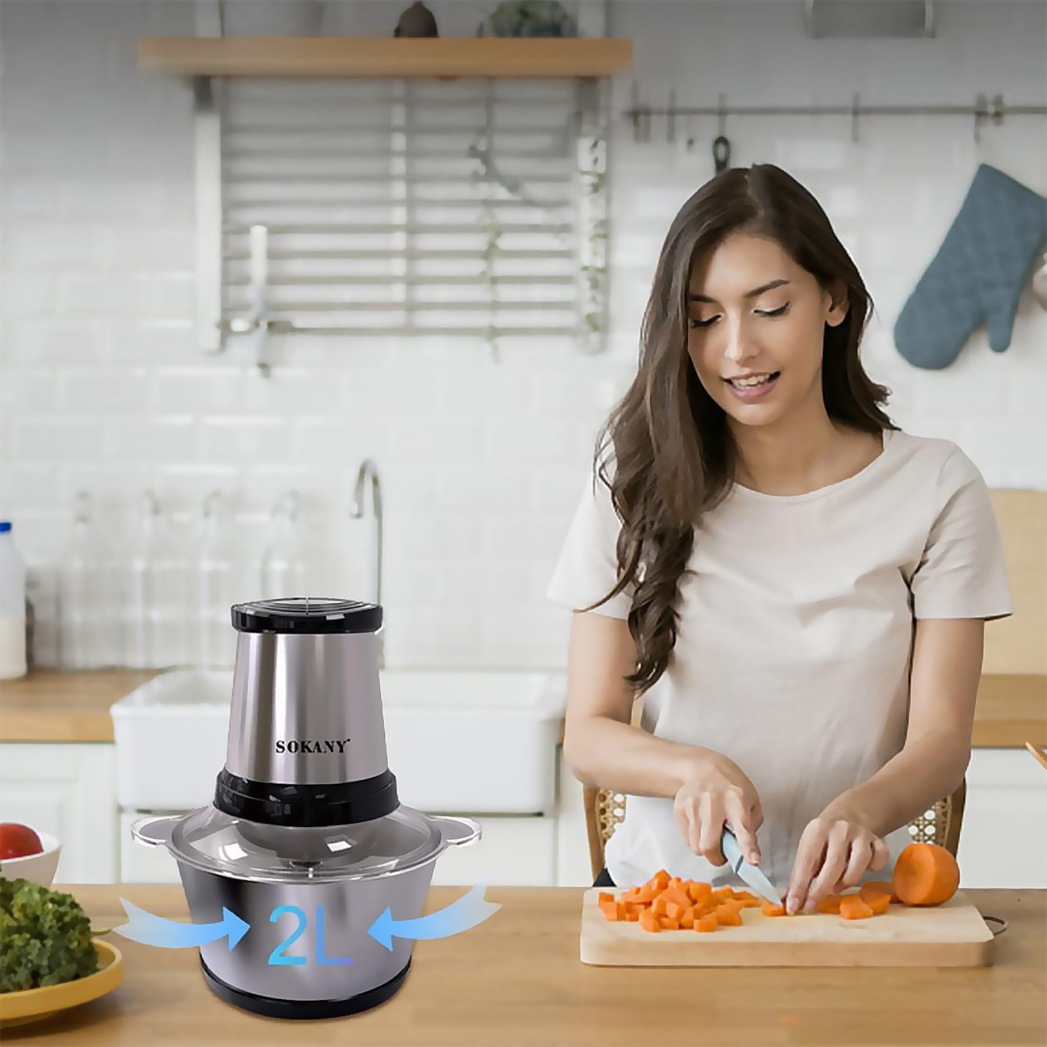 Una donna taglia carote su un tagliere in legno in una cucina. Un robot da cucina è sul tavolo e c'è una ciotola di broccoli.