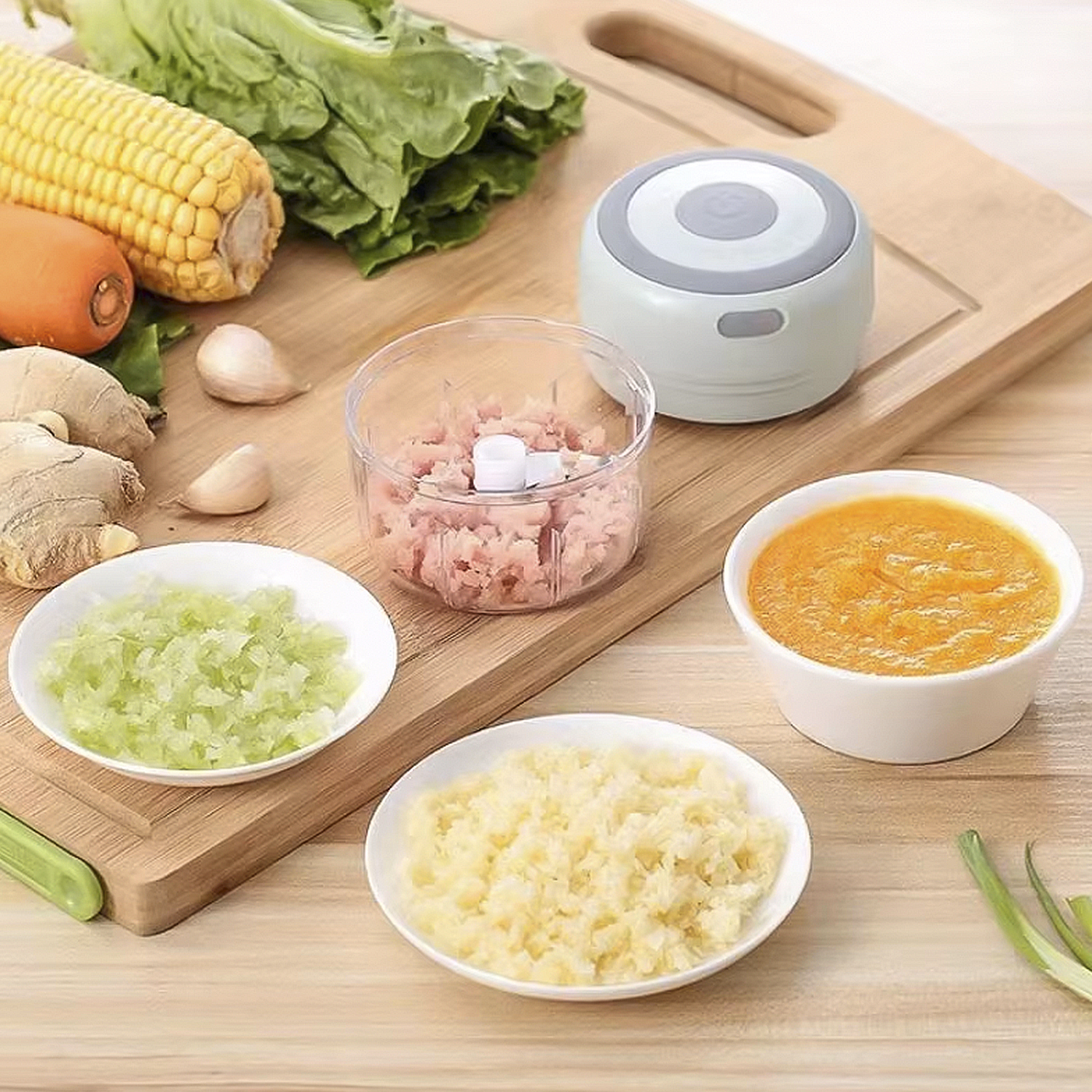 Un tagliere con verdure e un robot da cucina. Il cibo tritato è in ciotole, tra cui carne rosa e verdure gialle e verdi.