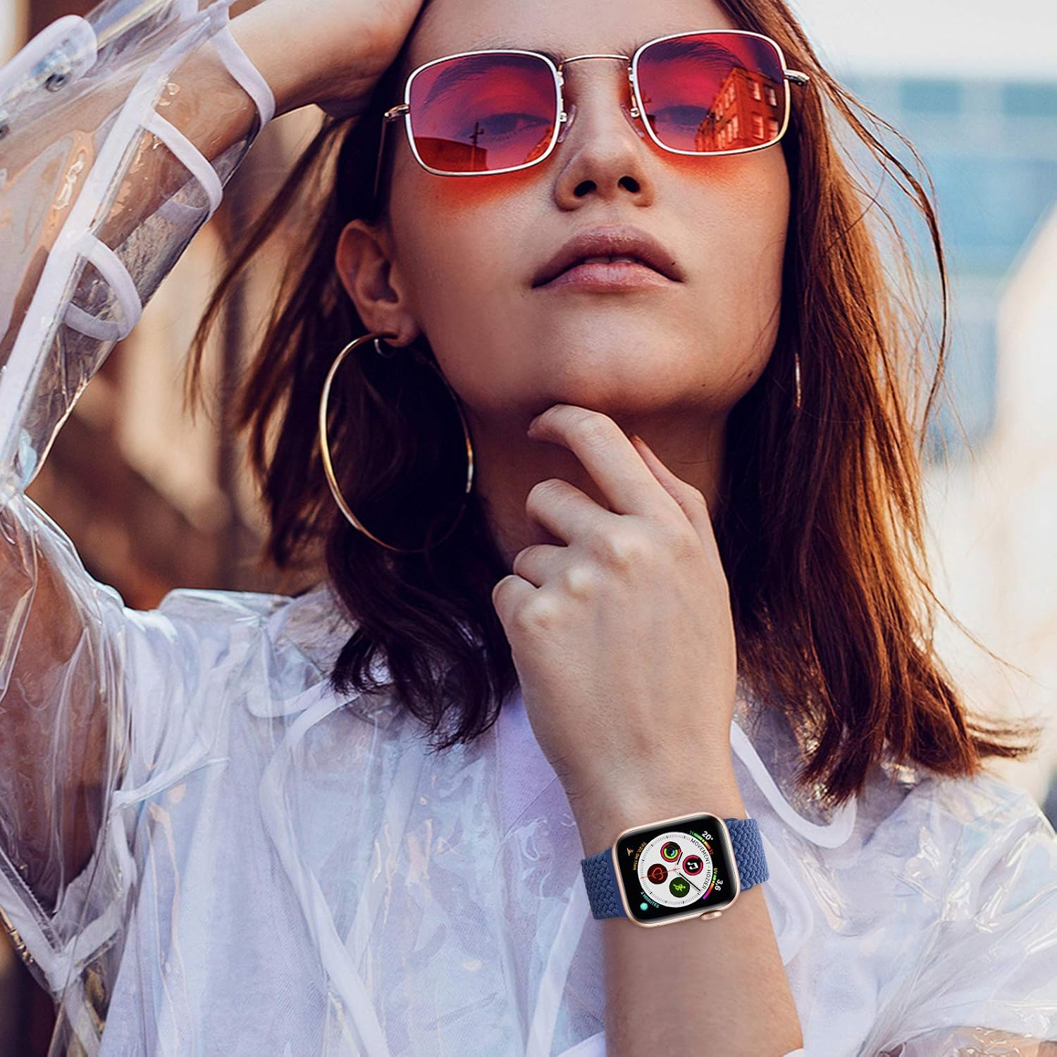 Frau mit roter Sonnenbrille, goldener Uhr mit blauem Armband und goldenen Reifen. Sie trägt eine transparente Jacke.