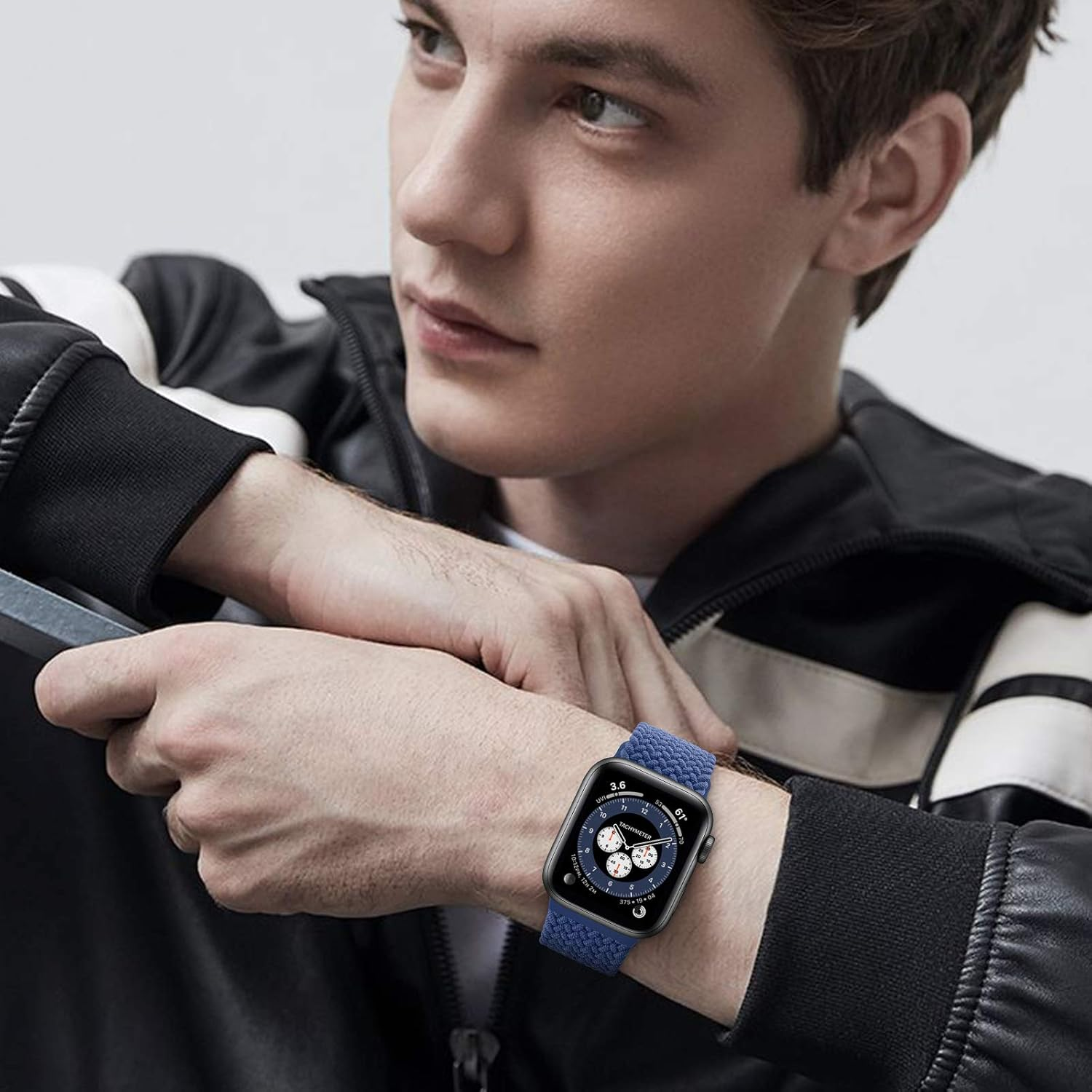 Ein Mann trägt eine schwarze Smartwatch mit blauem Armband und eine schwarze Jacke. Er schaut weg.