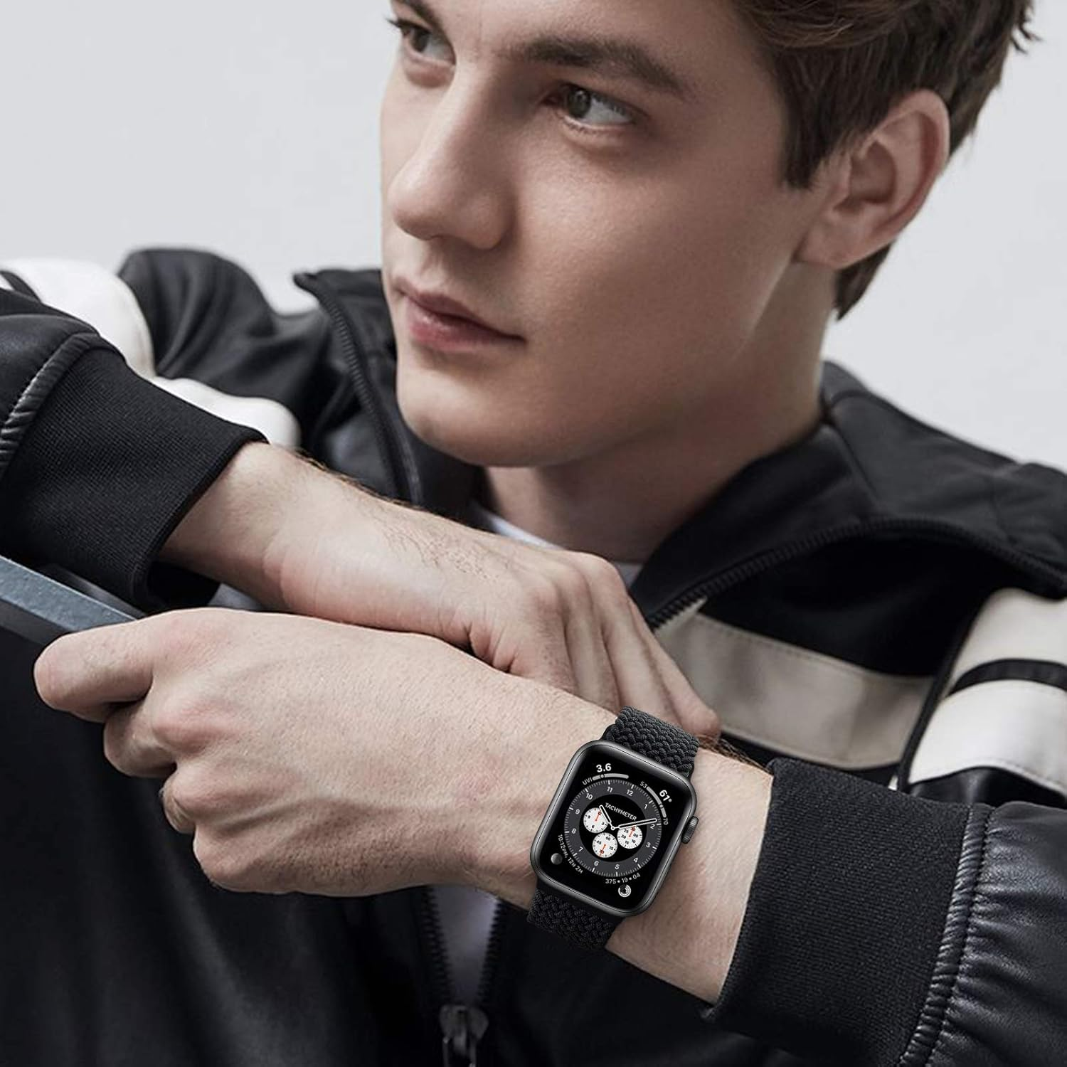 Ein Mann trägt eine schwarze Smartwatch mit gewebtem Armband. Das Zifferblatt zeigt Zahlen und Zifferblätter. Er trägt eine schwarze Jacke.