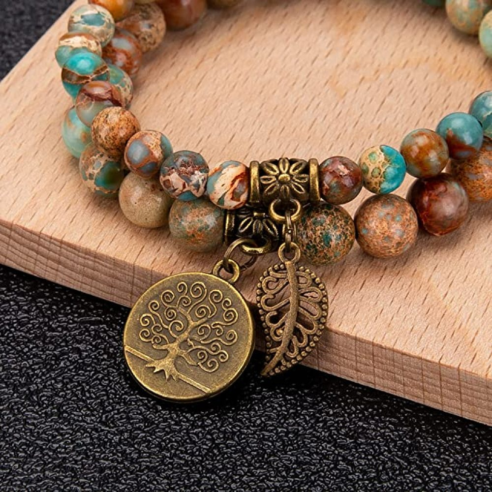 Ein Perlenarmband mit Baum- und Blattanhängern liegt auf einem Holzblock. Die Perlen sind braun, blaugrün und beige. Der Hintergrund ist schwarz.