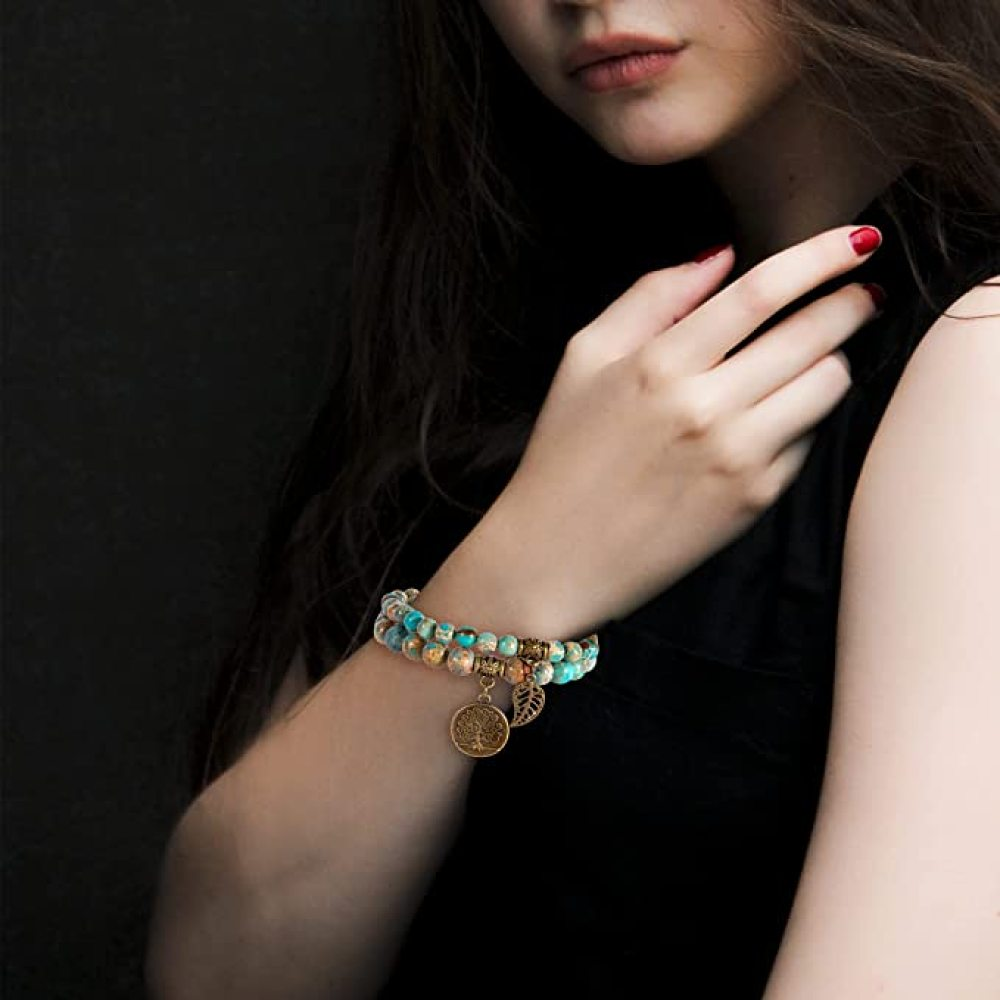 Eine Frau trägt ein Armband mit Perlen und einem Baum-Anhänger. Das Armband hat blaue, braune und goldene Perlen. Ihre Nägel sind rot lackiert.