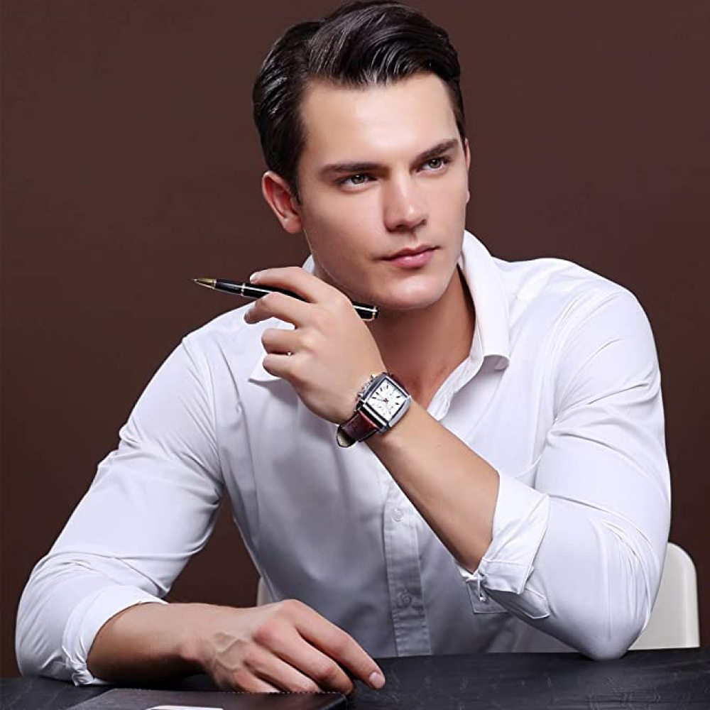 Ein Mann im weißen Hemd hält einen Stift und trägt eine Uhr. Er sitzt und wirkt nachdenklich. Der Hintergrund ist braun.
