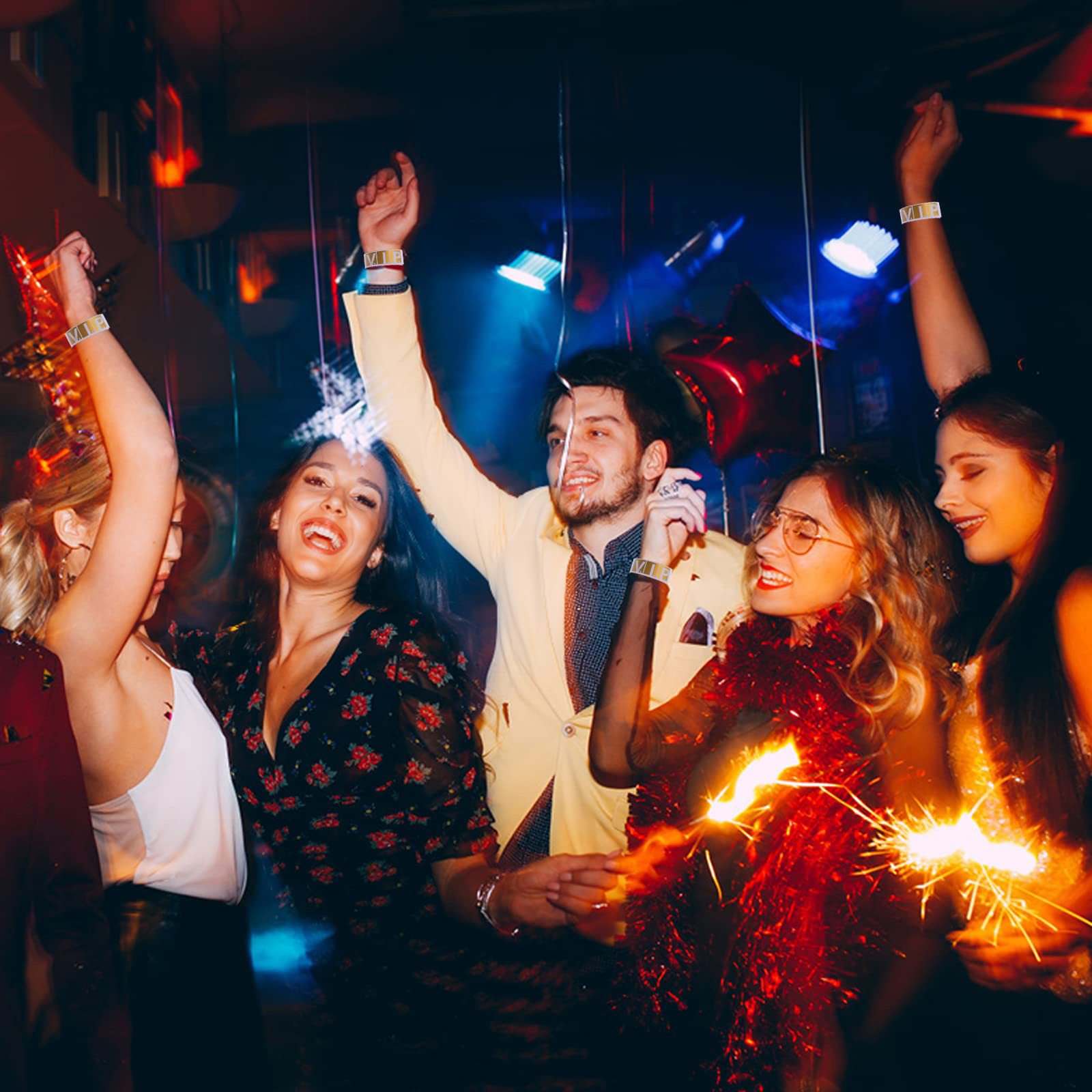 Menschen tanzen auf einer Party, halten Wunderkerzen und tragen VIP-Armbänder. Einige lächeln. Der Hintergrund ist dunkel.