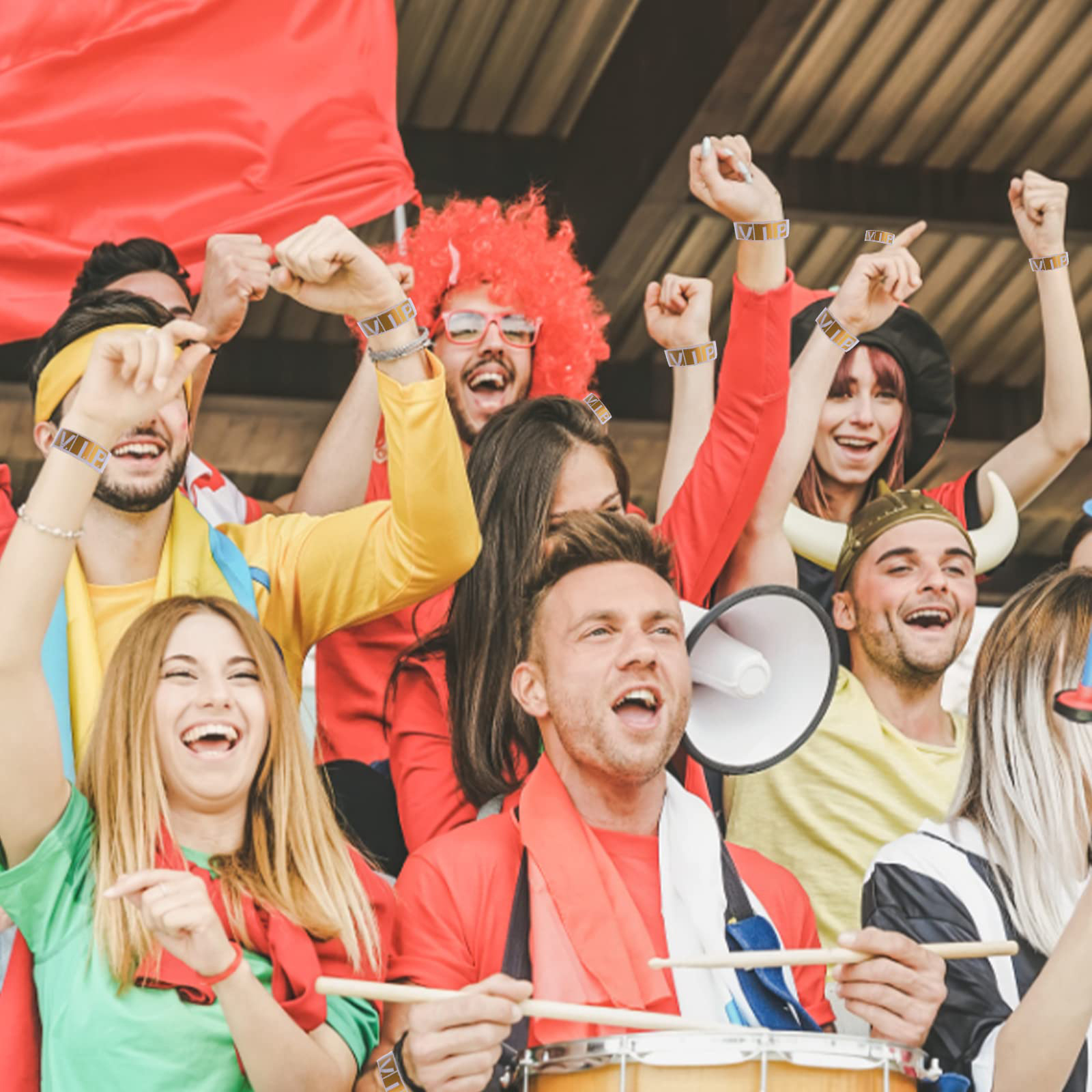 Eine Gruppe von Fans jubelt bei einer Sportveranstaltung, mit roter, gelber und grüner Kleidung. Einige haben VIP-Armbänder.