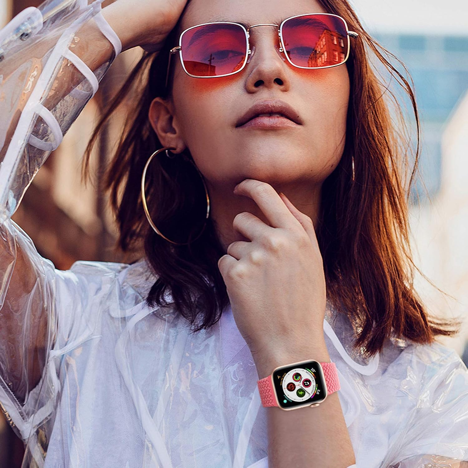 Frau mit Sonnenbrille, Uhr am Handgelenk und klarer Jacke. Sie berührt ihr Gesicht. Der Hintergrund ist unscharf.