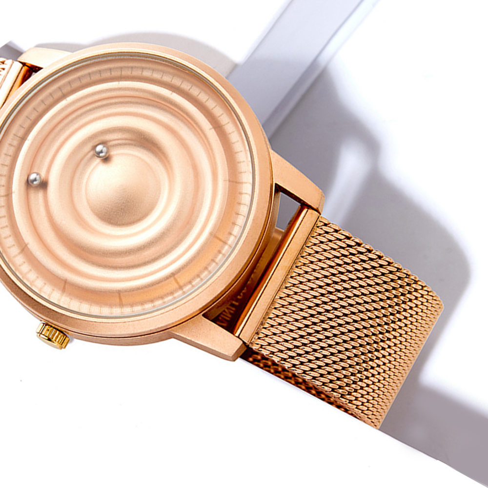 Roségold-Uhr mit einzigartigem Zifferblatt. Zwei kleine Kugeln zeigen die Zeit an. Mesh-Armband. Vor weißem und grauem Hintergrund.