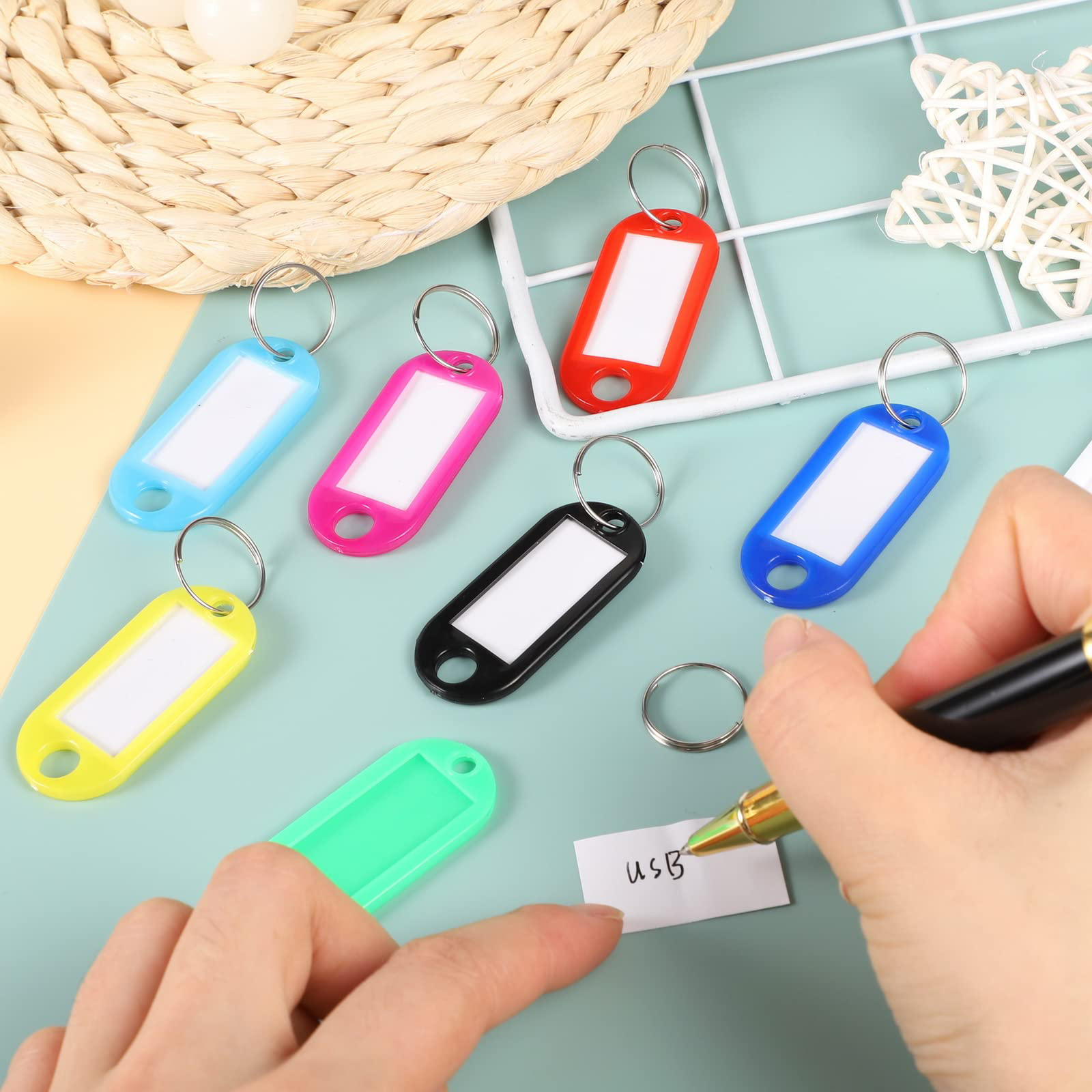 Bunte Schlüsselanhänger mit Etiketten liegen auf einem Tisch. Eine Hand schreibt auf ein Papier mit USB.