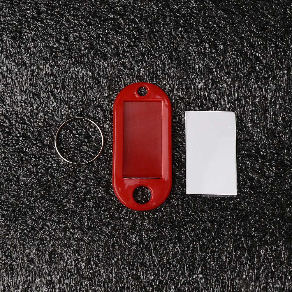 Ein roter Schlüsselanhänger, ein silberner Ring und ein weißes Rechteck liegen auf einer strukturierten schwarzen Oberfläche.