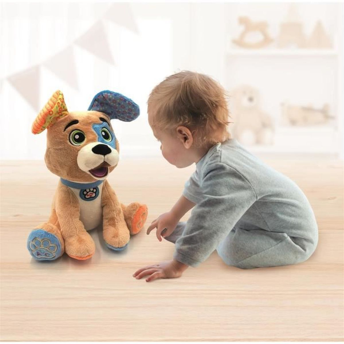 Ein Baby betrachtet einen Plüschhund. Der Hund ist braun, blau und orange. Das Baby trägt einen grauen Strampler.