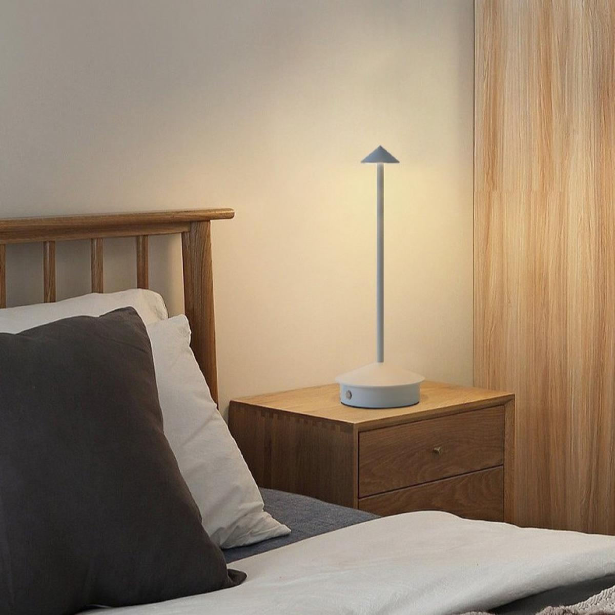 Schlafzimmer mit Bett, Kissen, Nachttisch und Lampe. Die Lampe ist beleuchtet.