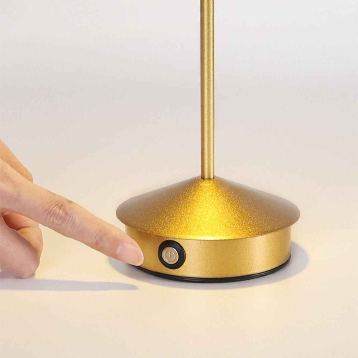 Eine Hand drückt einen Ein- und Ausschalter an einer goldenen Lampenbasis. Die Lampe hat einen goldenen Stiel und einen Lampenschirm.
