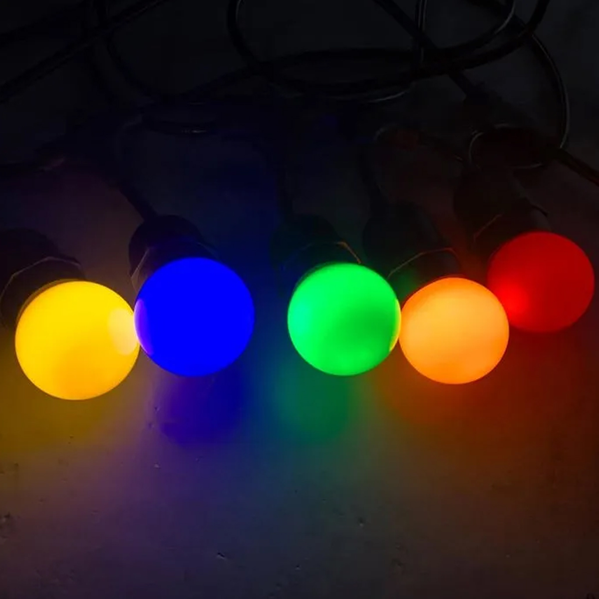 Reihe farbiger Lichter: gelb, blau, grün, orange und rot, vor dunklem Hintergrund, mit Drähten darüber.