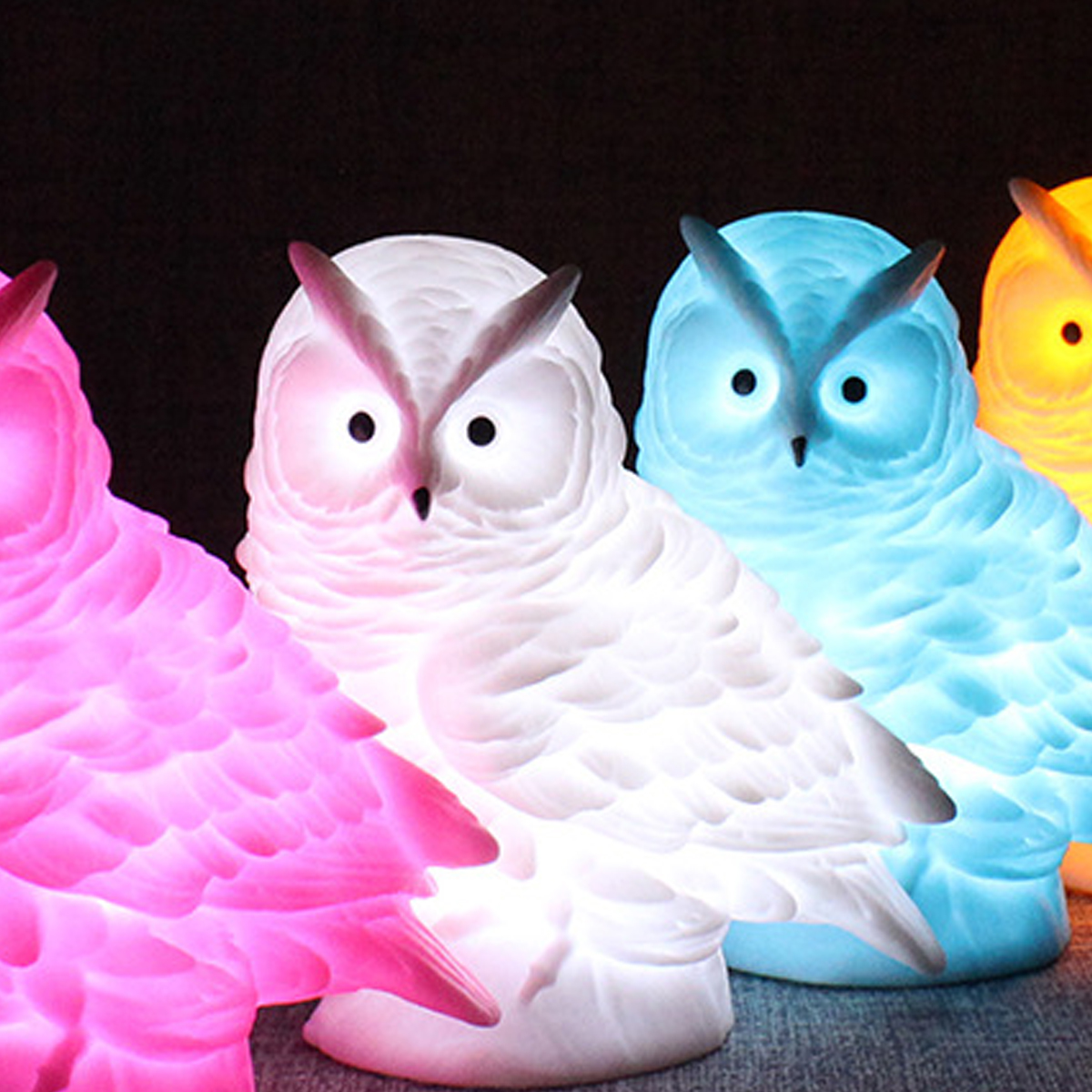 Vier bunte eulenformige Lampen. Von links: rosa, weiß, blau und gelb. Sie leuchten, mit schwarzem Hintergrund.