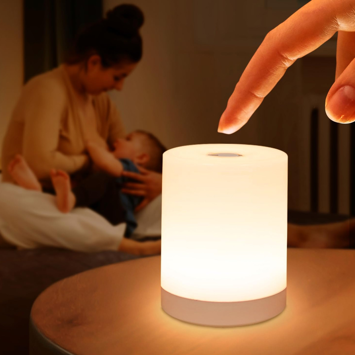 Auf einem Tisch steht eine leuchtende zylindrische Lampe. Ein Finger berührt sie fast. Im Hintergrund stillt eine Mutter ein Baby.