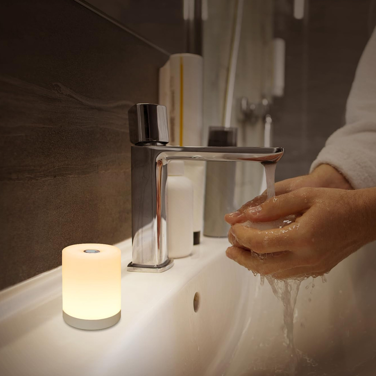 Eine Person wäscht sich die Hände in einem Badezimmer. Eine leuchtende Lampe steht auf dem Waschbecken, neben dem Wasserhahn und Flaschen.