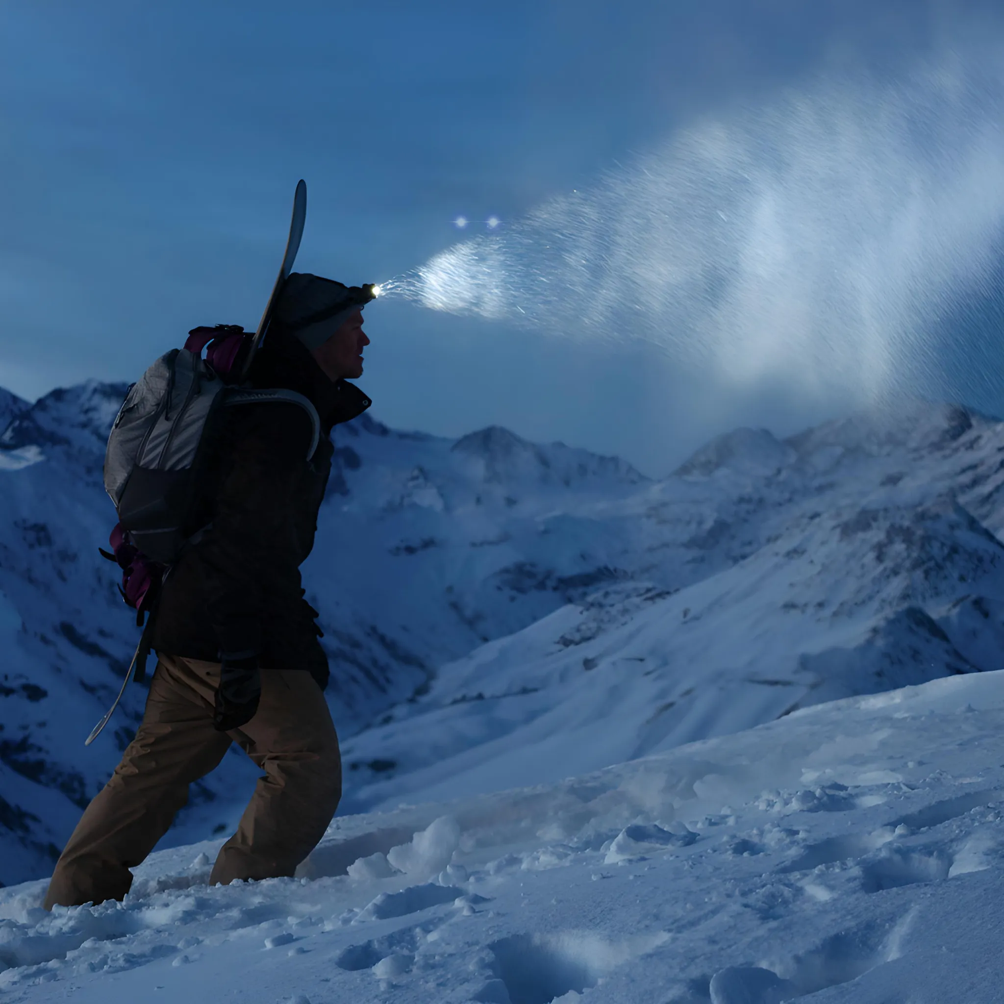 Skifahrer mit Stirnlampe und Snowboard auf verschneitem Berg bei Nacht. Stirnlampenstrahl reflektiert Schnee.