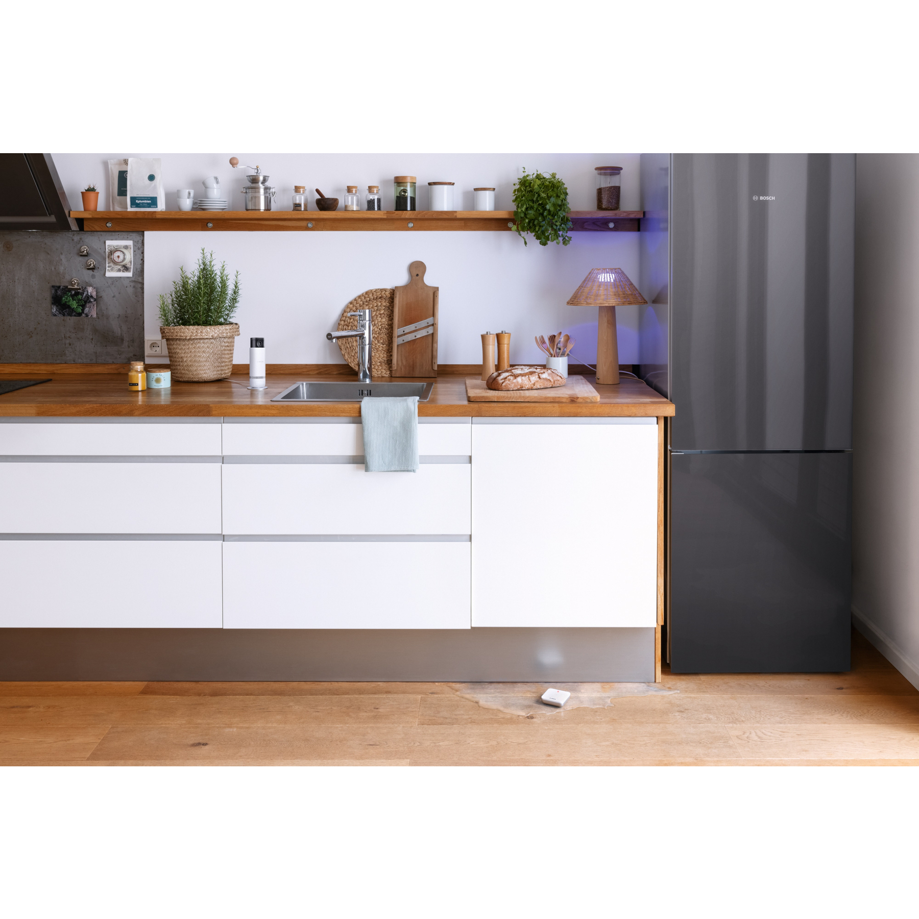 Eine moderne Küche mit grauem Kühlschrank, Holzarbeitsplatten, weißen Schränken und Regalen mit Gewürzen und Pflanzen.