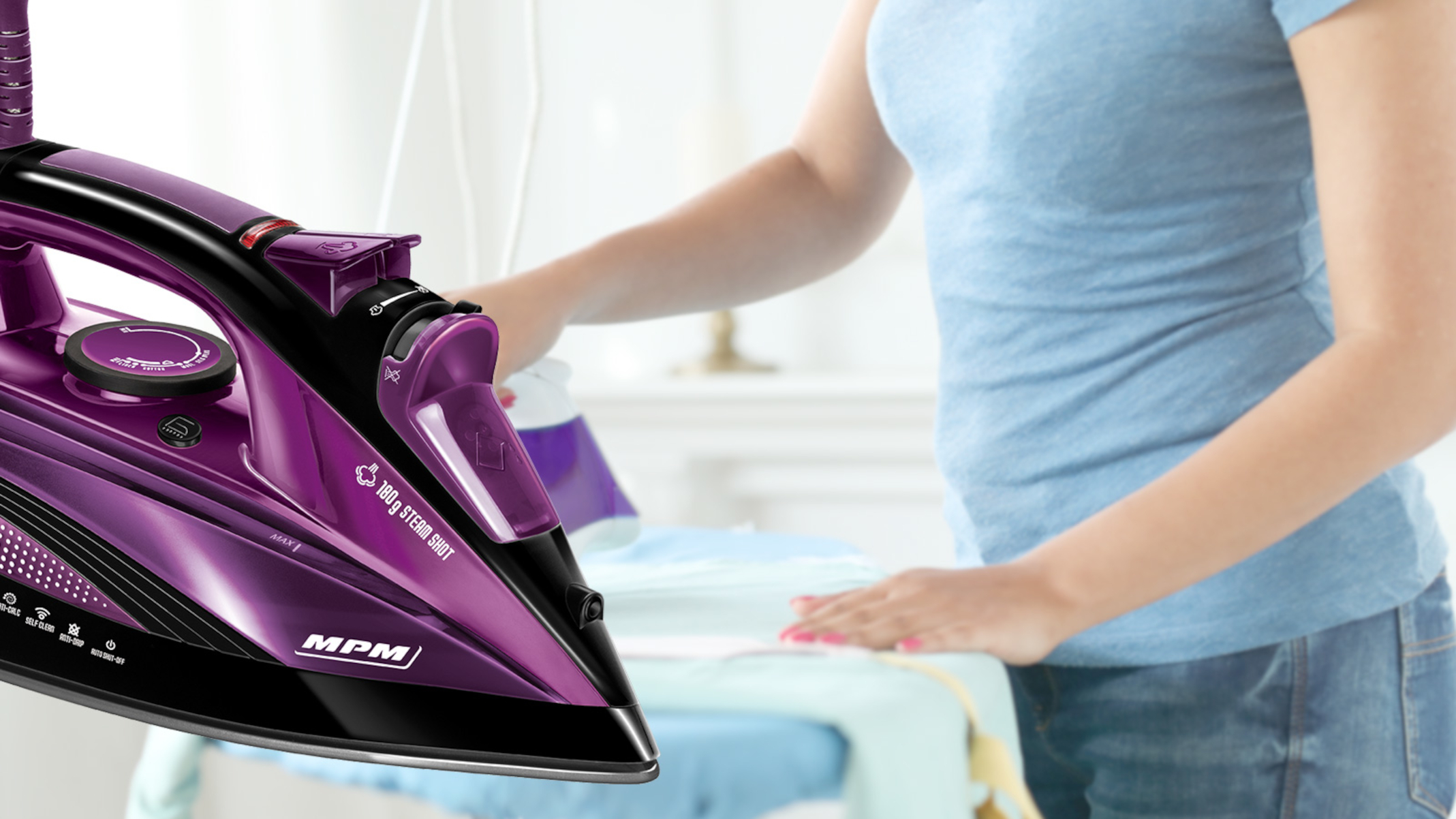 Kobieta prasuje ubrania fioletowym żelazkiem. Żelazko jest ostre, kobieta jest w tle. Scena jest w pomieszczeniu.