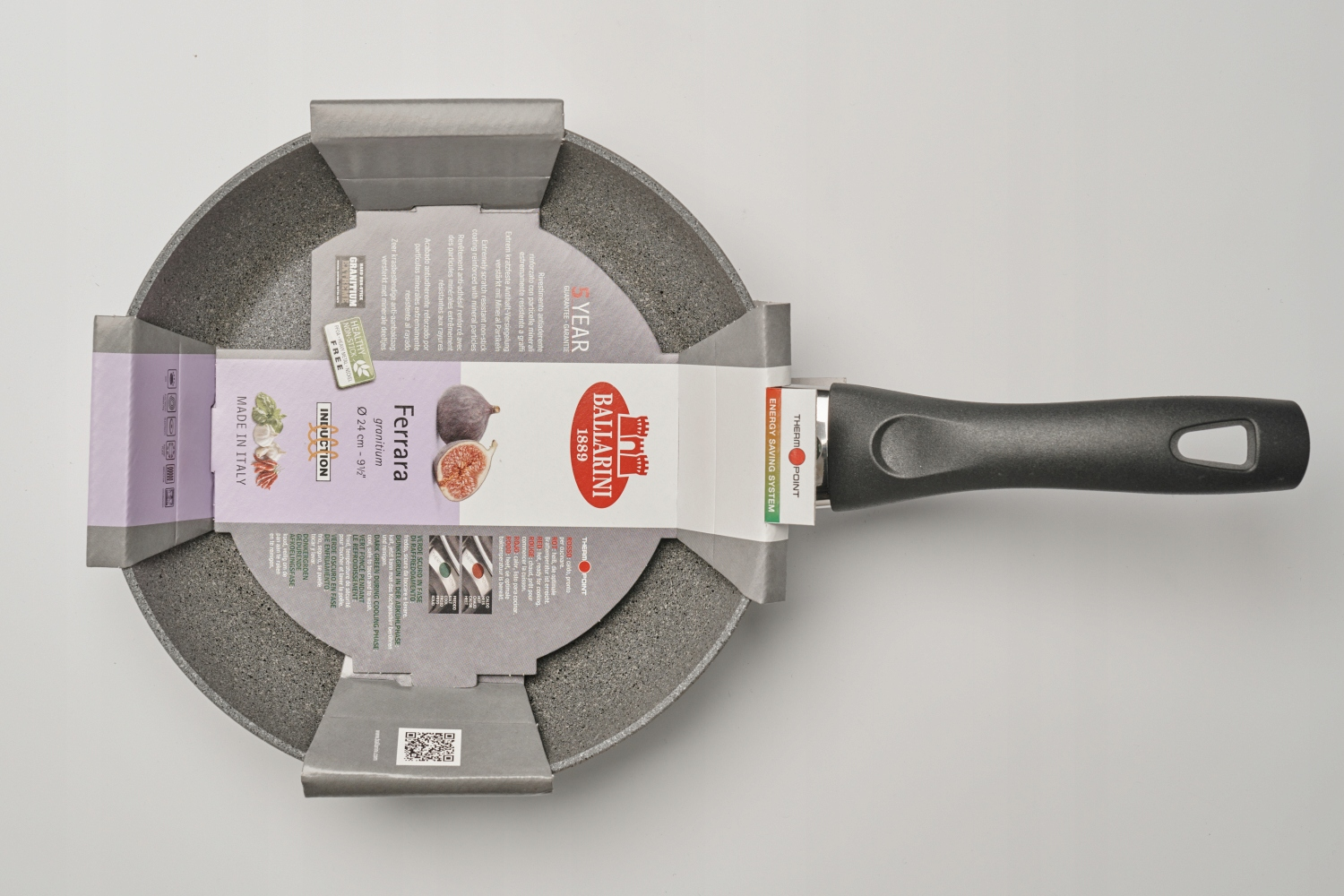 Nowa patelnia granitowa Ballarini Ferrara z czarnym uchwytem na białej powierzchni. Opakowanie otacza patelnię.