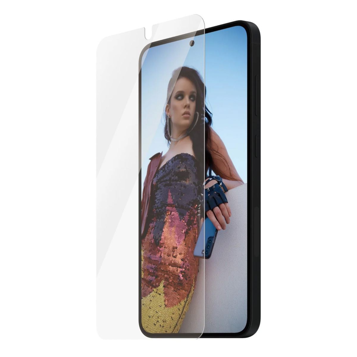 Un teléfono con protector de pantalla muestra a una mujer con un vestido de lentejuelas y chaqueta. La mujer sostiene un teléfono y se apoya en una pared blanca.