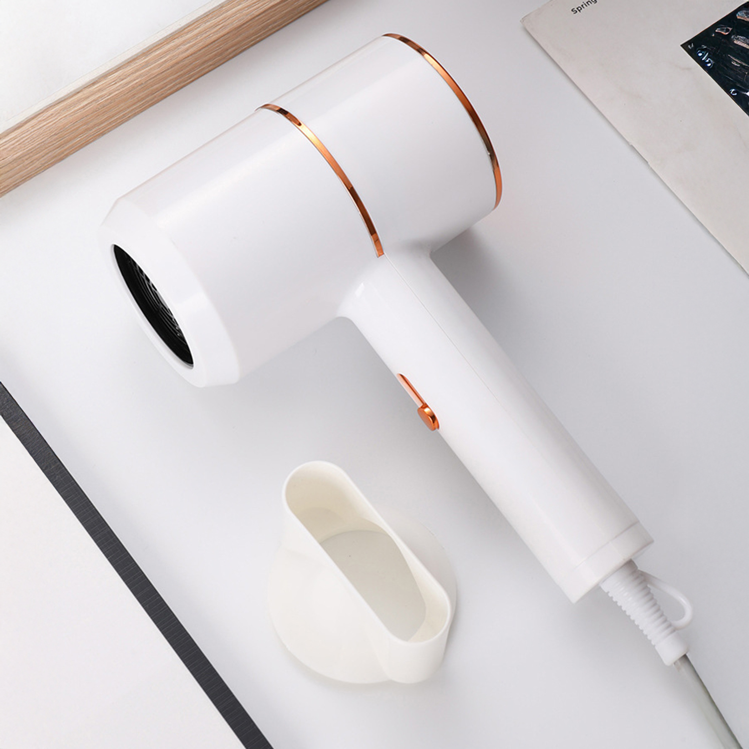 Un asciugacapelli bianco e rame con un supporto bianco su una superficie bianca. Sono presenti anche una cornice in legno e una rivista.