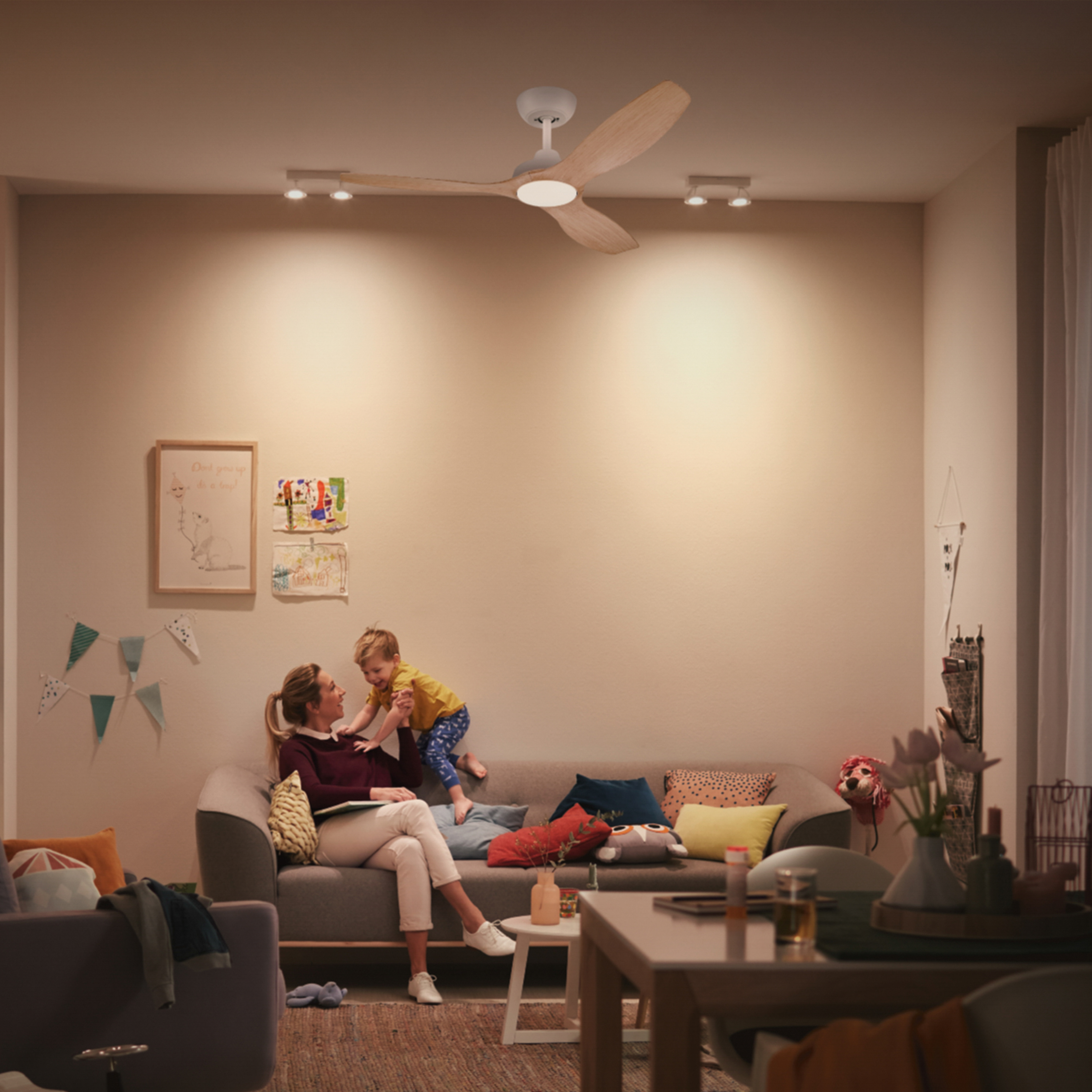 Una mujer y un niño en un sofá en una habitación iluminada. Ventilador de techo y obras de arte.