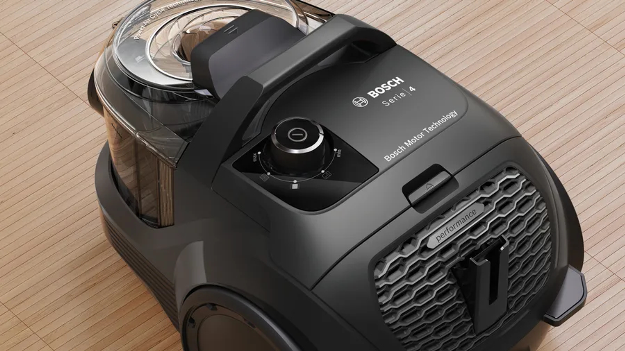 Czarny odkurzacz Bosch. Posiada uchwyt, pokrętło sterowania i filtr powietrza. Umieszczony na drewnianej podłodze.