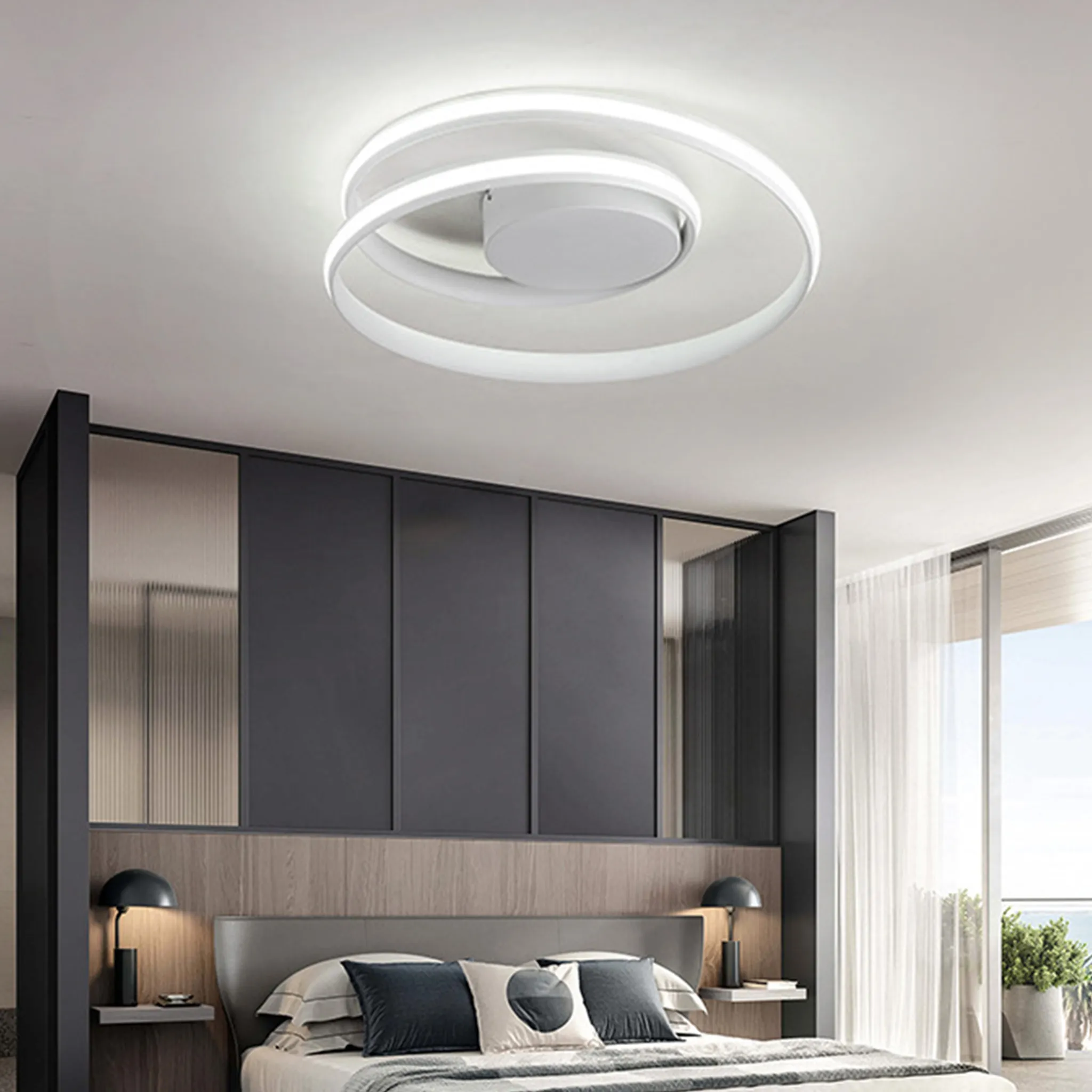Schlafzimmer mit spiralförmiger Deckenleuchte. Ein Bett, ein dunkelgraues Kopfteil und ein großes Fenster sind sichtbar.