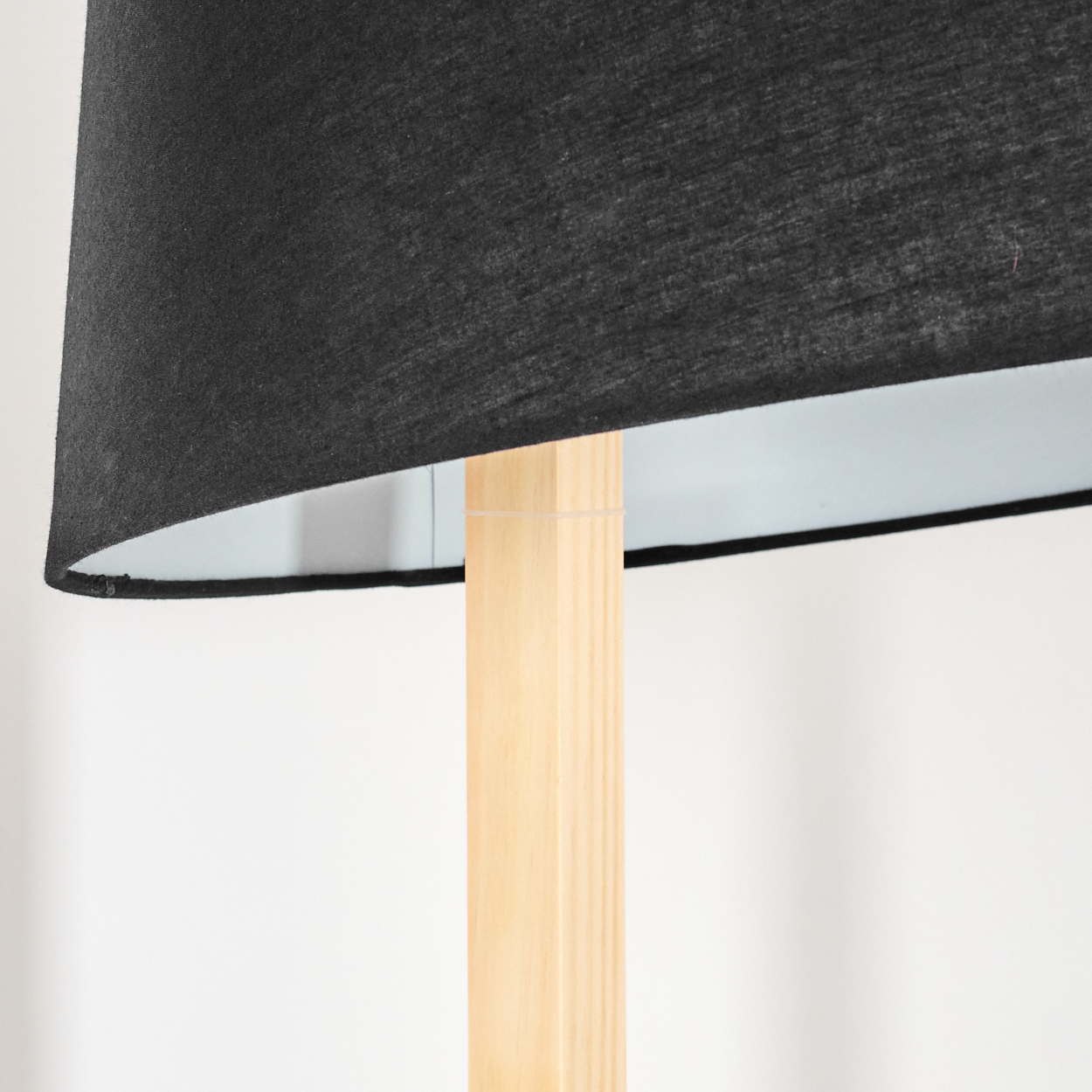 Nahaufnahme einer Lampe. Schwarzer Lampenschirm über einem hellen Holzständer. Weiße Wand im Hintergrund.