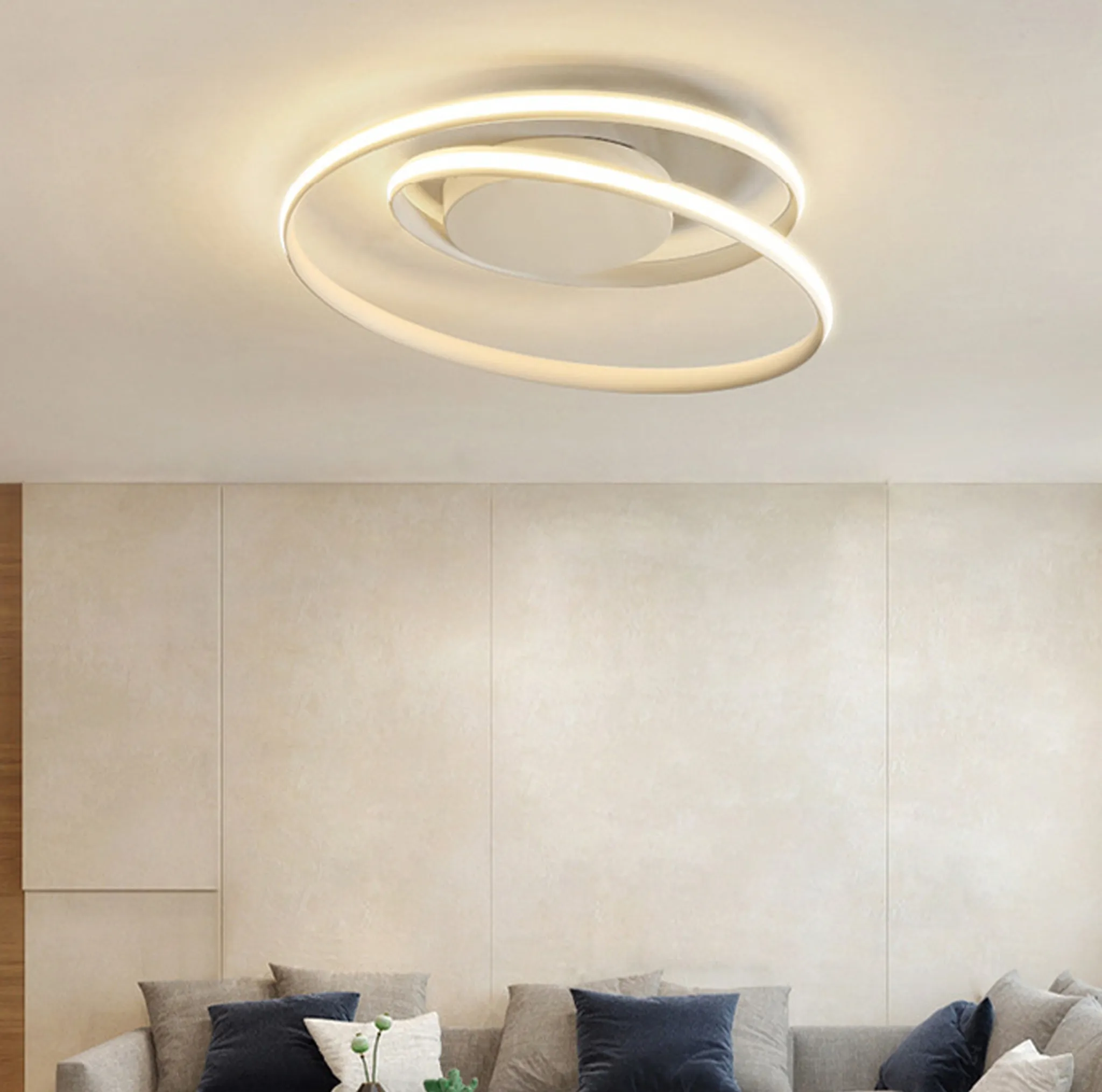 Eine moderne Deckenleuchte mit Spiraldesign beleuchtet ein Wohnzimmer. Ein Sofa und Wandpaneele sind darunter sichtbar.