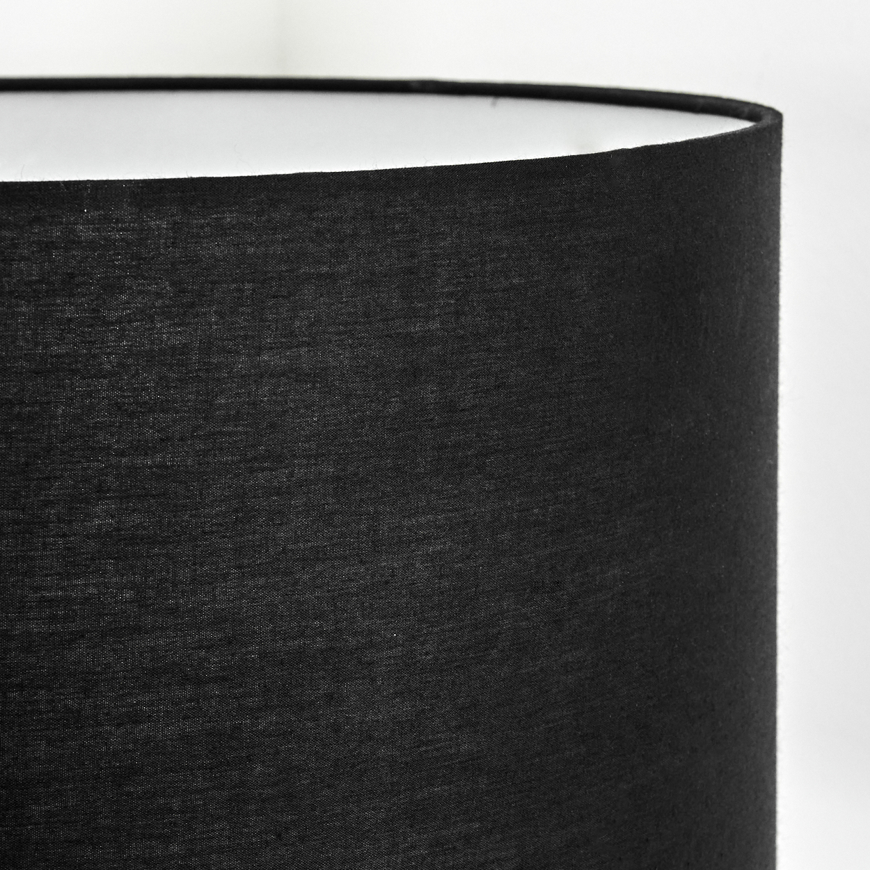 Nahaufnahme eines schwarzen Lampenschirms. Der Stoff hat Textur. Die Innenseite ist weiß, im Kontrast zu Schwarz. Hintergrund ist weiß.