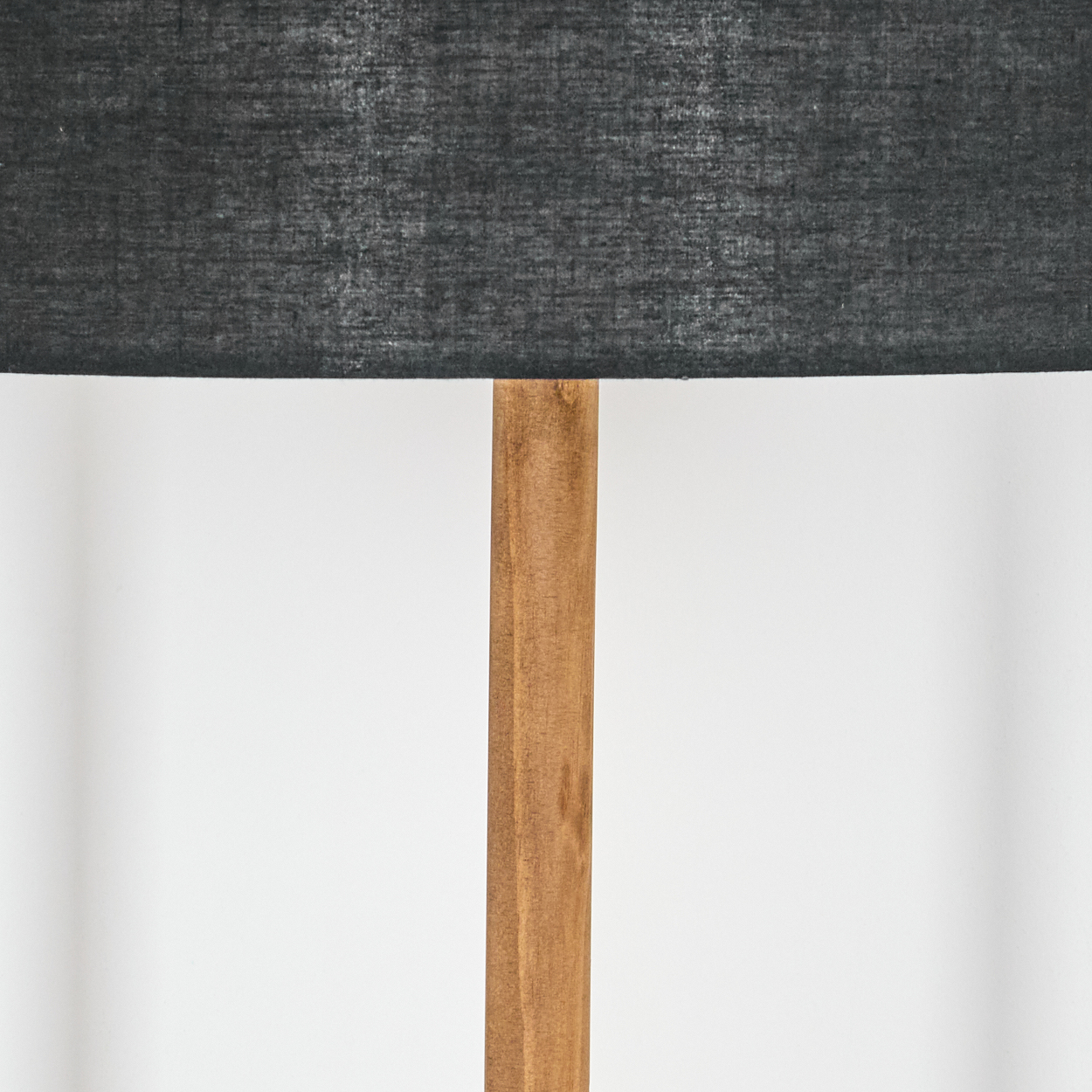 Nahaufnahme einer Lampe. Sie hat einen dunkelgrauen Lampenschirm und einen Holzpfahl. Der Hintergrund ist eine schlichte weiße Wand.