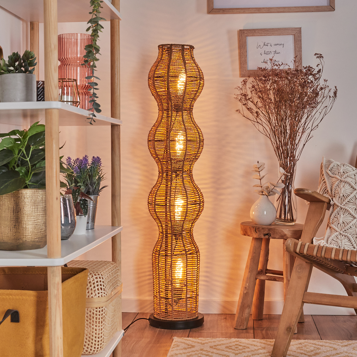 Eine gewebte Stehlampe leuchtet, umgeben von Regalen mit Pflanzen und Dekoration. Rechts steht ein Holzstuhl mit Kissen.