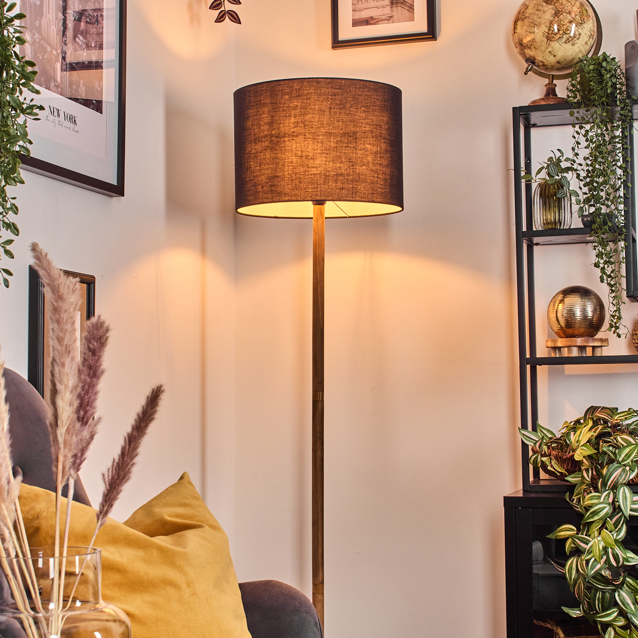 Eine Stehlampe mit dunklem Schirm steht in einer Ecke. Ein Regal mit Deko und ein New York-Poster sind sichtbar.