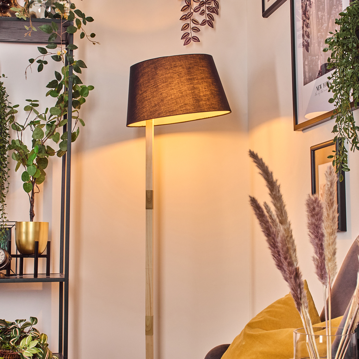 Eine beleuchtete schwarze Lampe steht neben einer Wand. Pflanzen und gerahmte Bilder sind im Hintergrund.