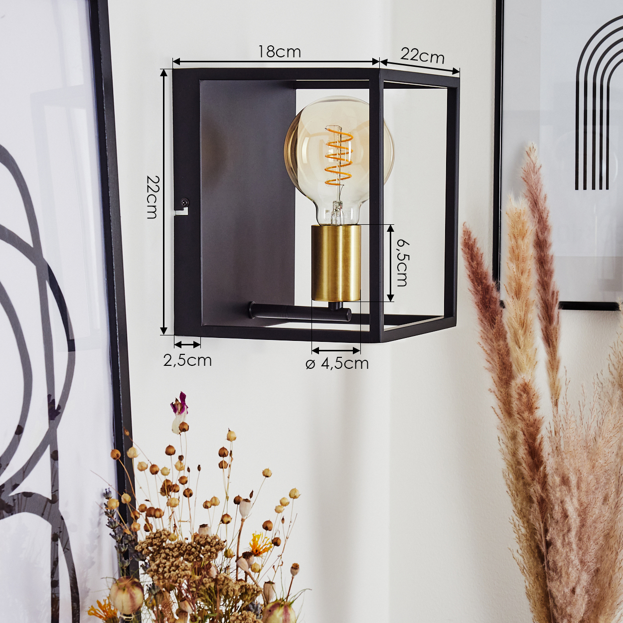 Eine schwarze Wandlampe mit goldenem Leuchtmittelhalter. Maße sind angegeben. Trockenblumen sind im Vorder- und Hintergrund.
