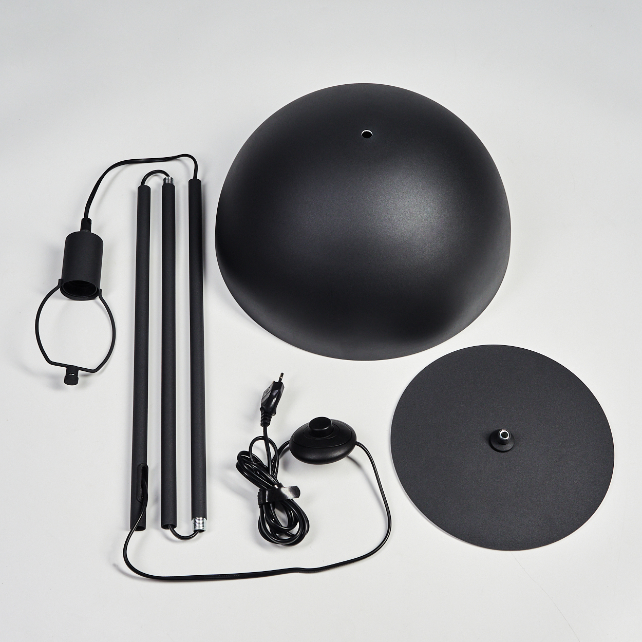 Schwarze Stehlampenteile: Basis, Schirm, Stangen, Kabel mit Schalter und eine runde Basis auf weißer Oberfläche.