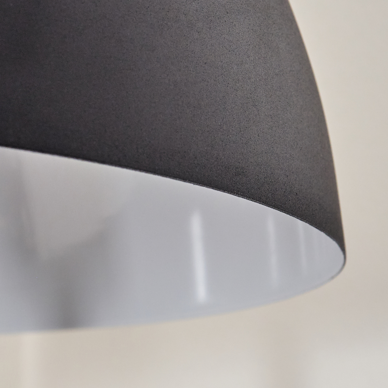 Nahaufnahme eines schwarzen Lampenschirms mit weißem Innenraum. Der Lampenschirm ist strukturiert und der Hintergrund ist ein verschwommenes Beige.