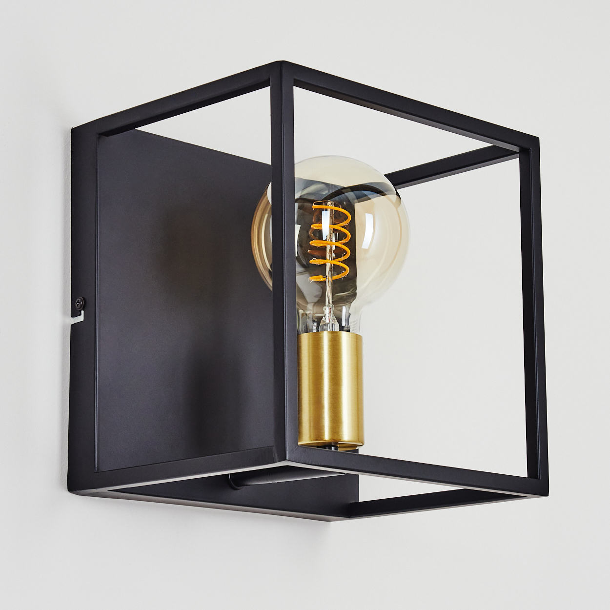 Eine moderne schwarze Metall-Wandleuchte mit goldenem Sockel und Glühbirne in einem quadratischen Rahmen an einer weißen Wand.