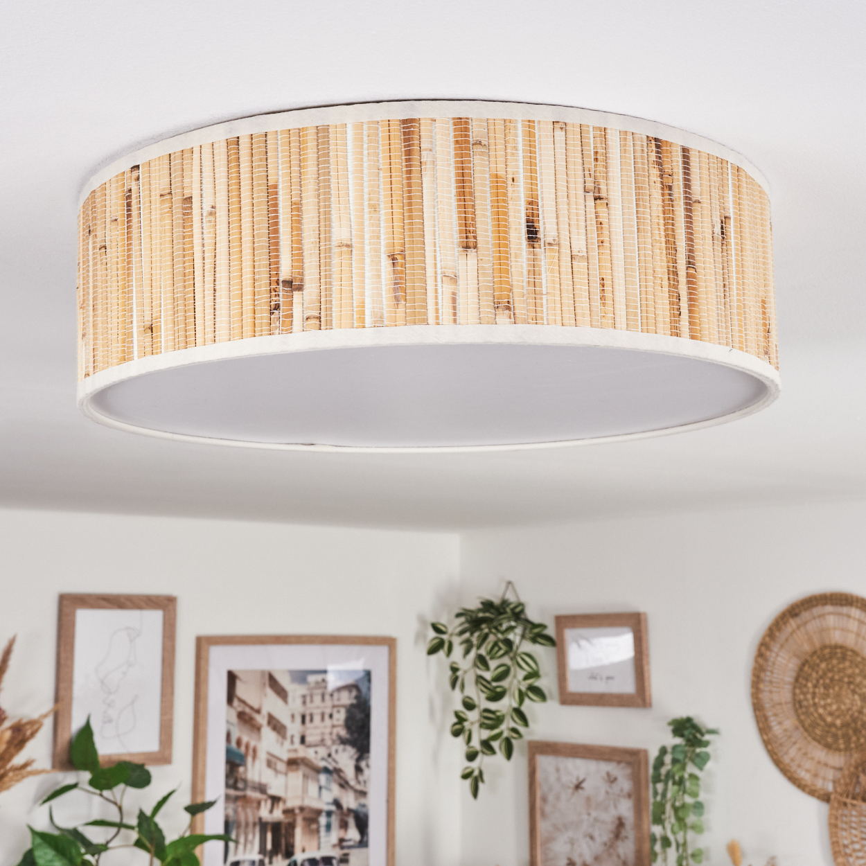 Eine runde Deckenlampe mit Bambusschirm. Darunter gerahmte Bilder, Pflanzen und eine Wanddekoration.