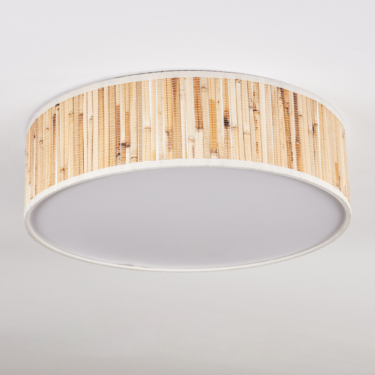 Eine runde Deckenlampe mit Bambus-Schirm. Die Lampe hat einen weißen, kreisförmigen Sockel und ist an einer weißen Decke befestigt.