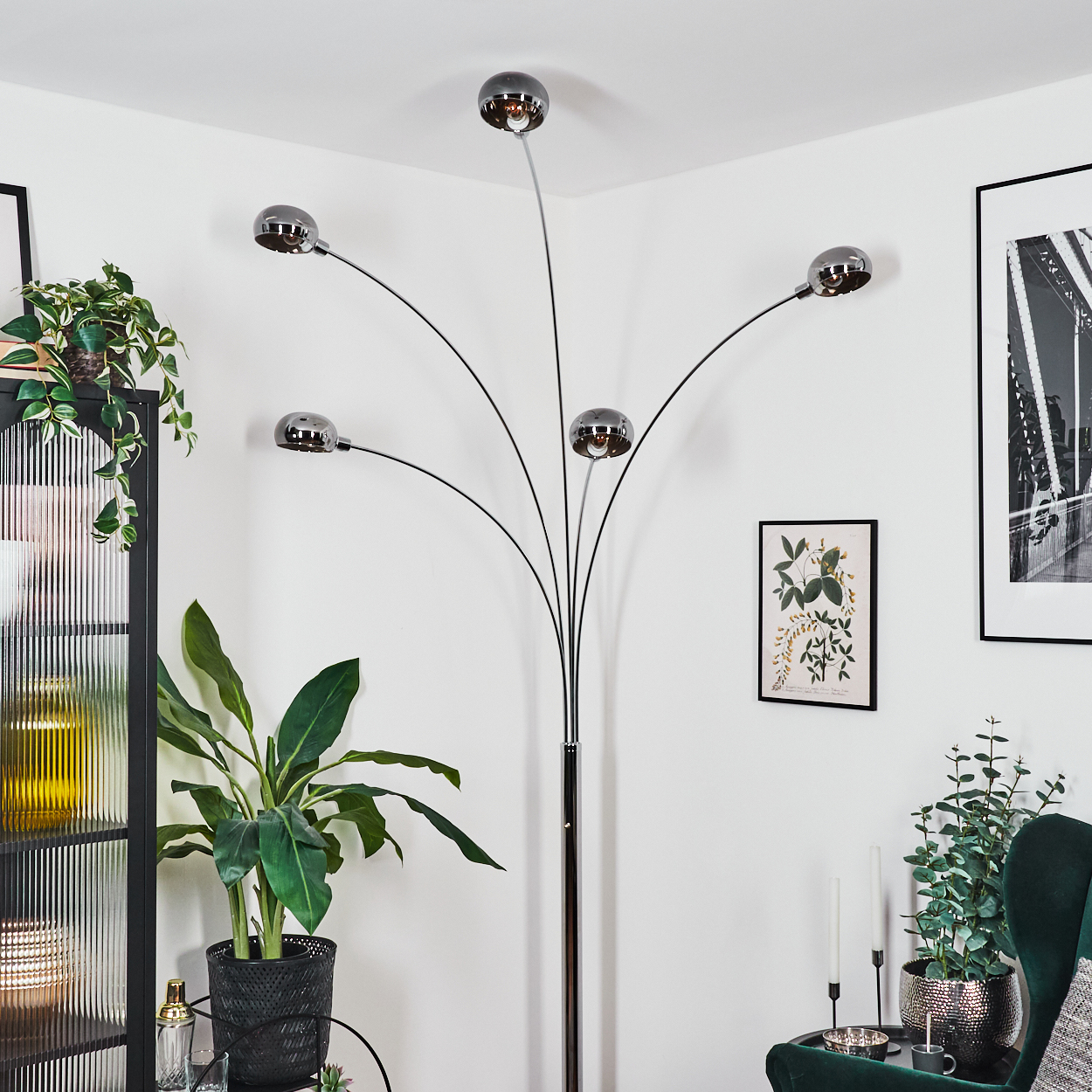 Ein modernes Wohnzimmer mit Stehlampe, Pflanzen, Kunstwerken und einem grünen Sessel.