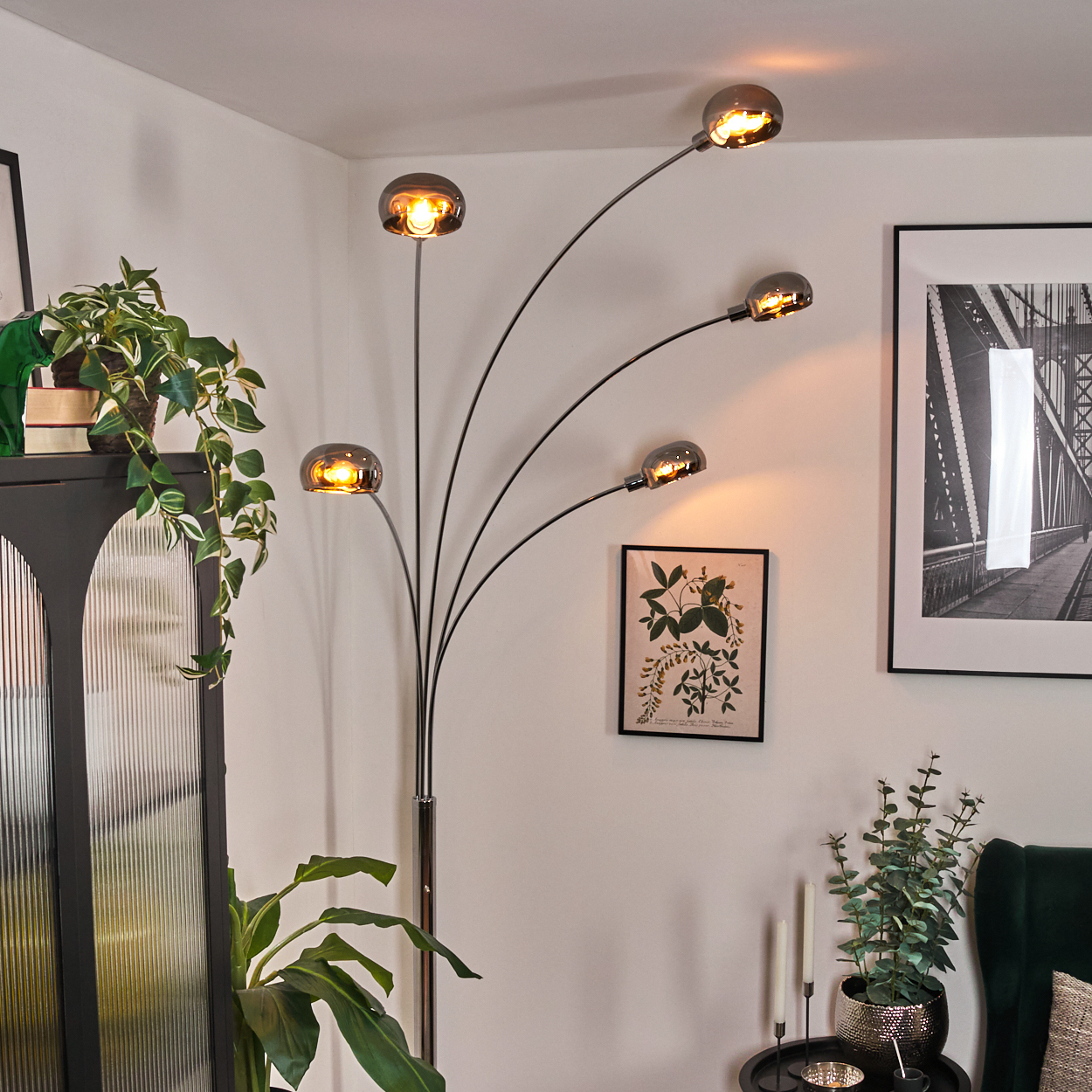 Ein modernes Wohnzimmer mit Stehlampe. Es gibt einen schwarzen Schrank mit Pflanzen, ein Brückenfoto und einen kleinen Tisch mit Kerzen.
