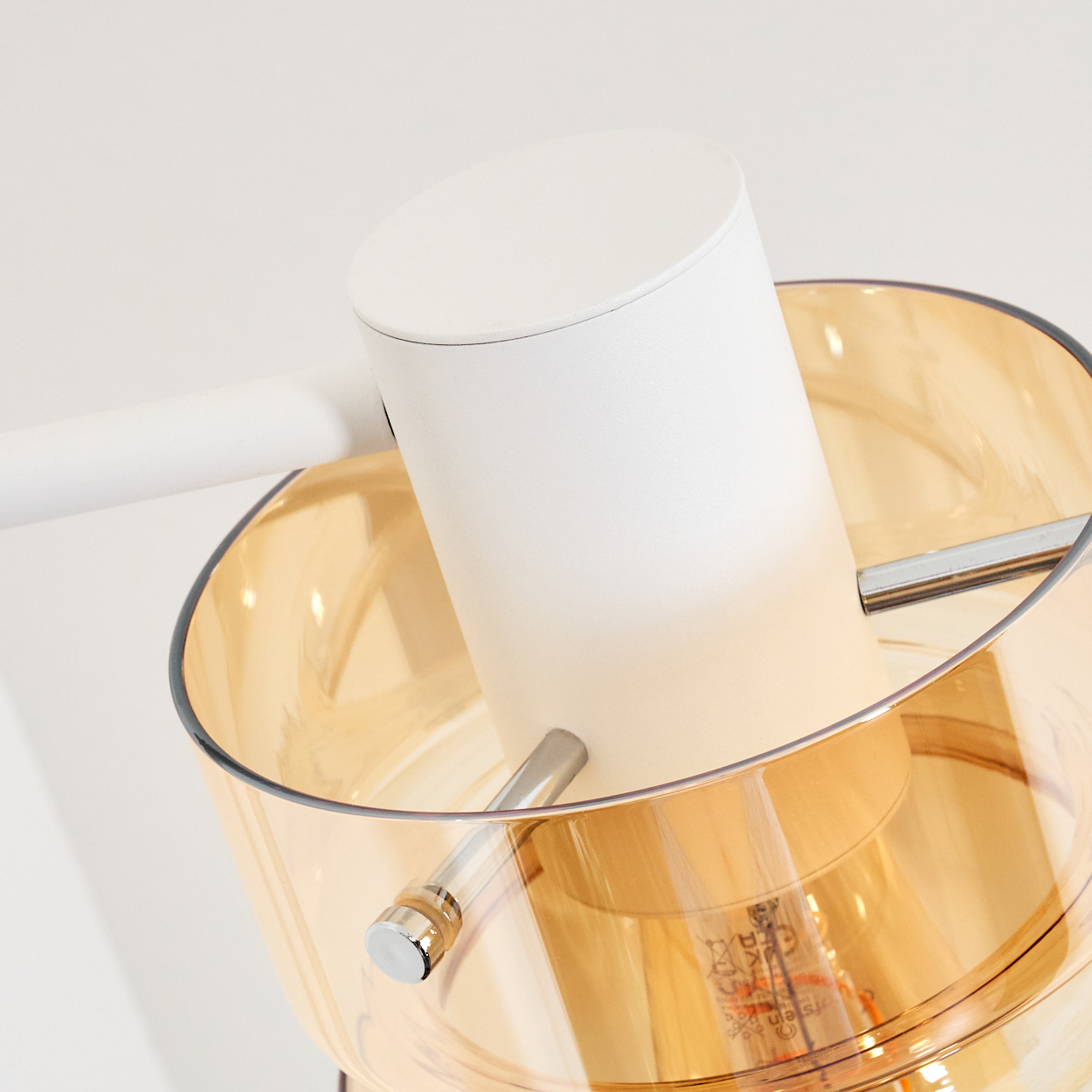 Eine moderne Lampe mit weißem zylindrischen Schirm über einer durchscheinenden bernsteinfarbenen Glasschale. Eine Glühbirne ist sichtbar.