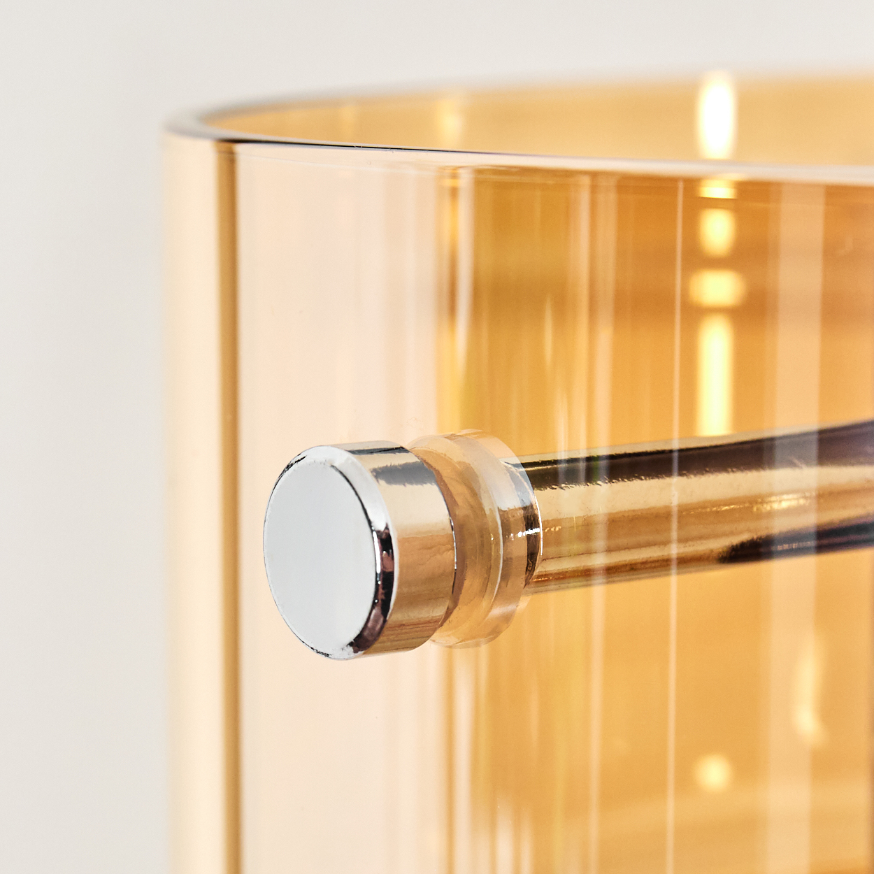 Nahaufnahme eines bernsteinfarbenen Glasbehälters mit einem Chromgriff. Der Hintergrund ist ein weiches, helles Creme.