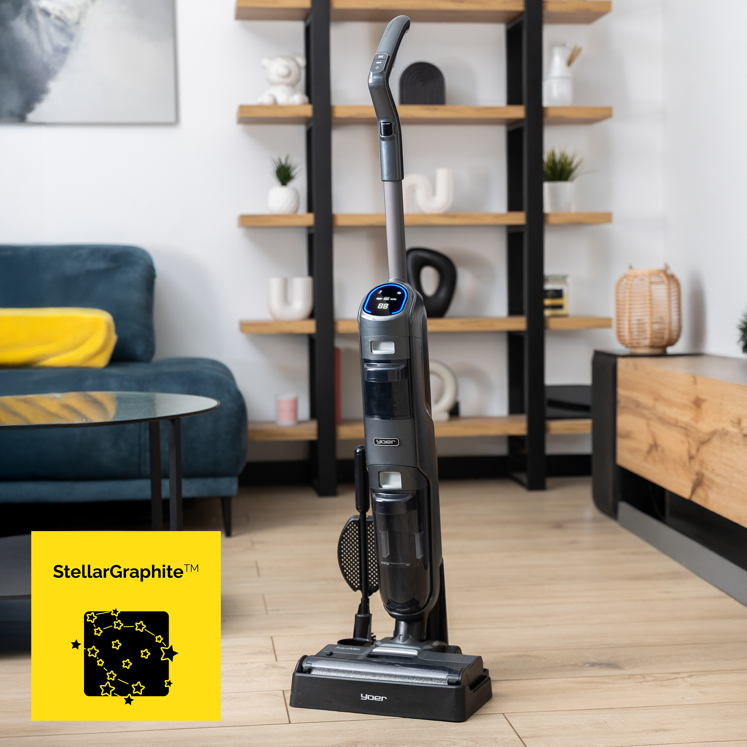 Czarny i szary odkurzacz stoi na drewnianej podłodze. Po lewej stronie znajduje się żółte logo.