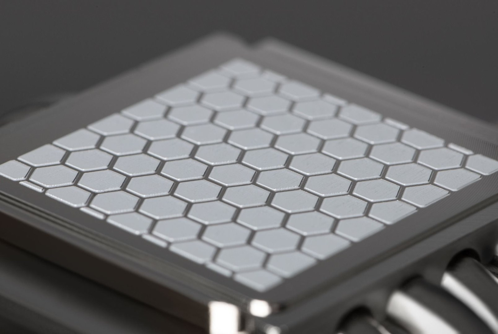 Zbliżenie srebrnego, geometrycznego wzoru plastra miodu na kwadratowej metalowej powierzchni z ciemnym tłem.